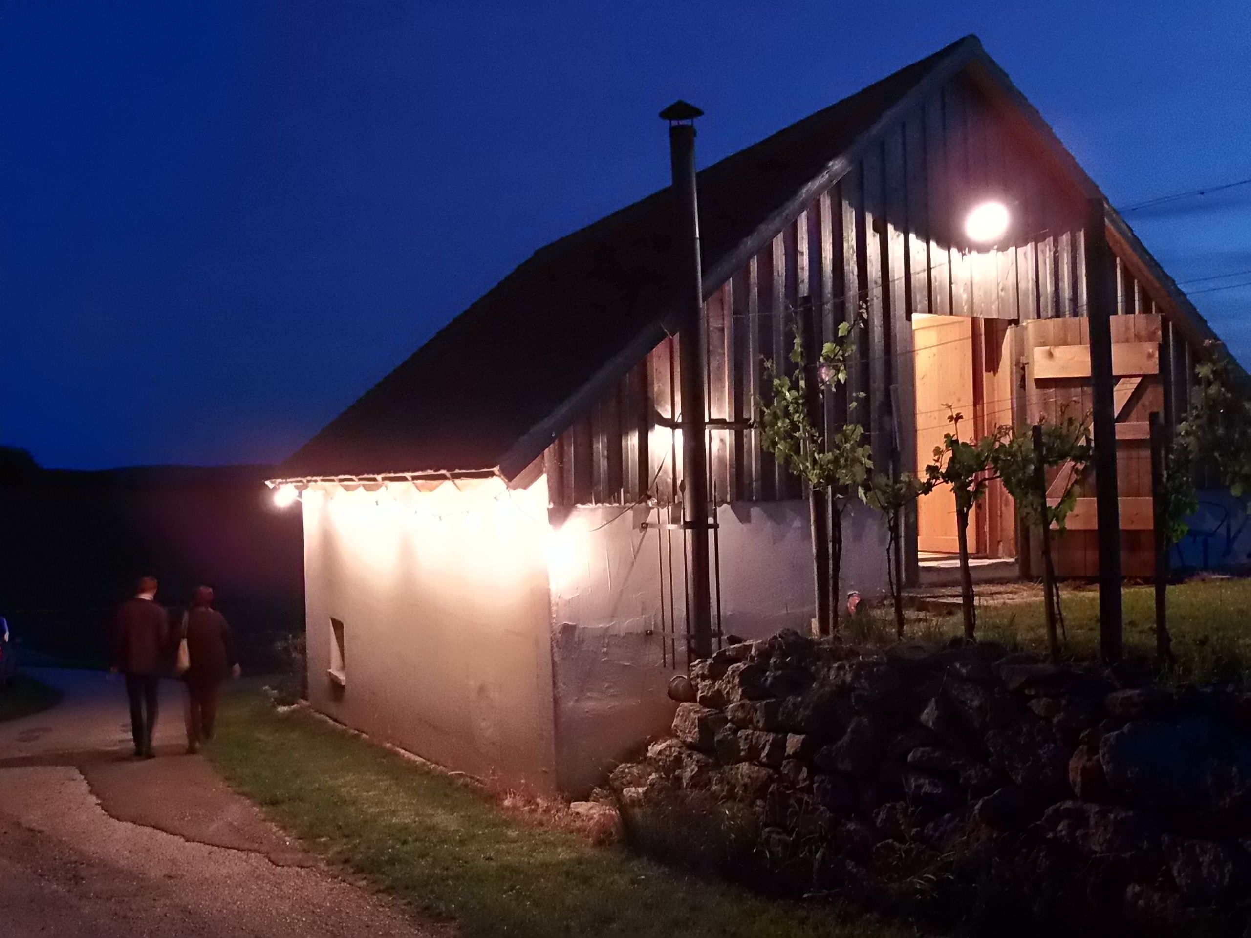 Osvětlená budova vinného sklepa v noci se dvěma lidmi na cestě.