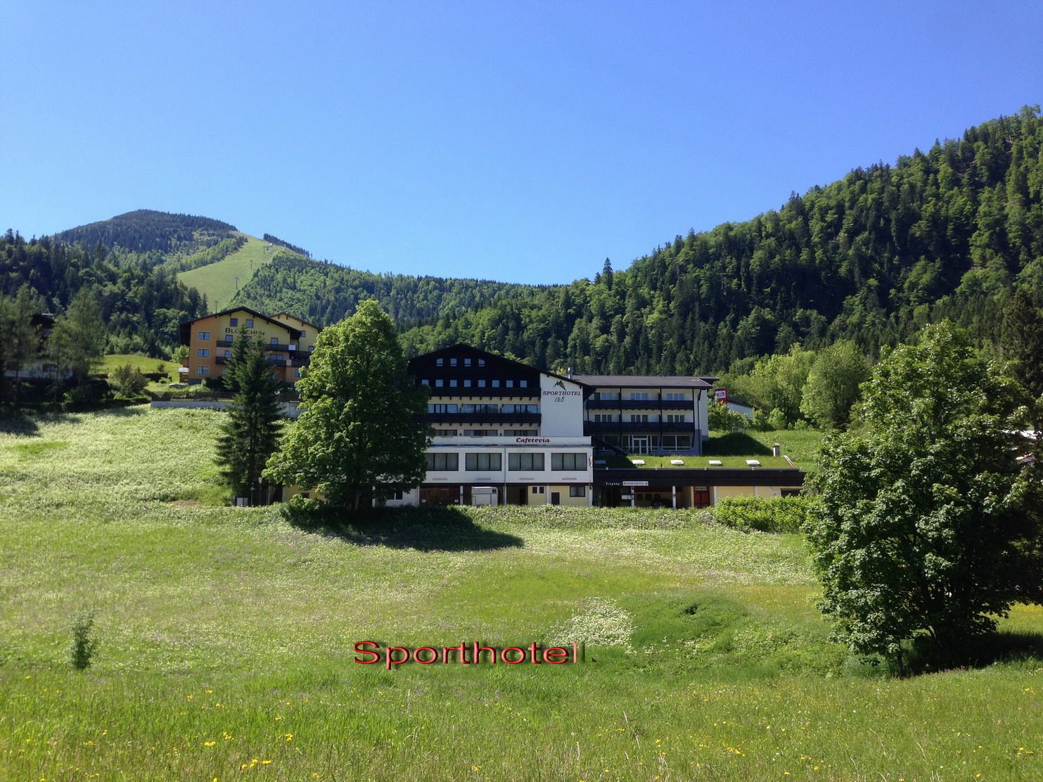 Sportovní hotel v zelené horské krajině s modrou oblohou.