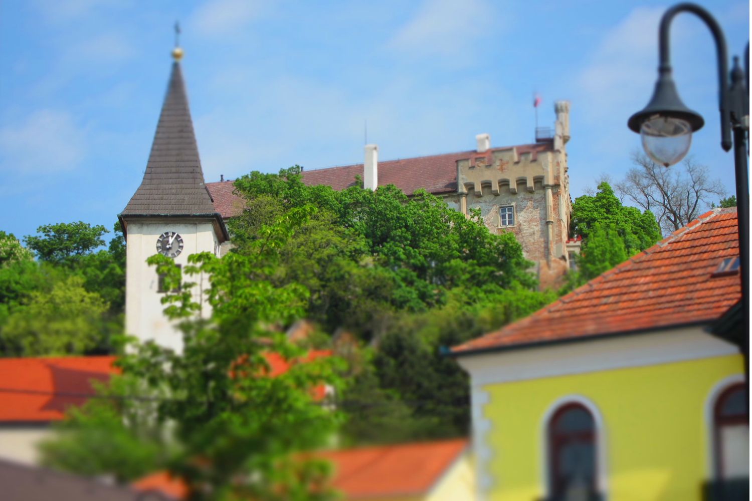 Kostelní věž a hrad za stromy, modrá obloha.