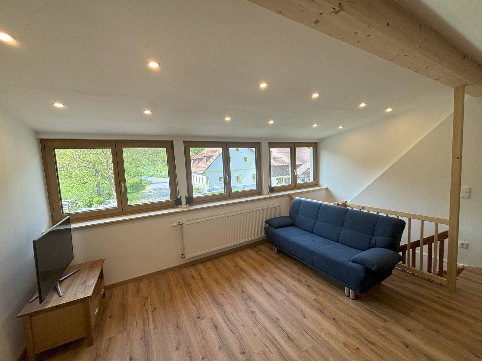 Obývací pokoj s modrou pohovkou, dřevěnou podlahou a velkými okny s výhledem ven.