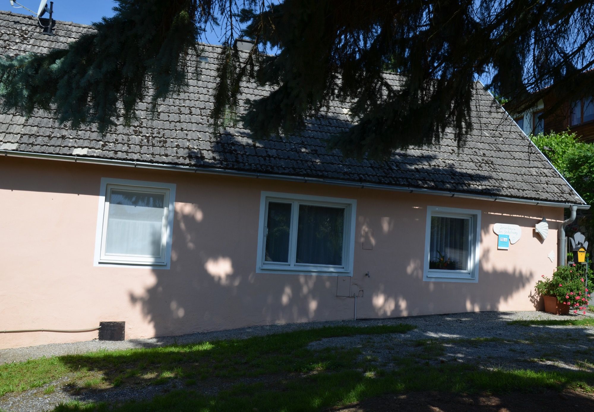 Malý růžový rekreační dům se stinnými stromy v popředí.