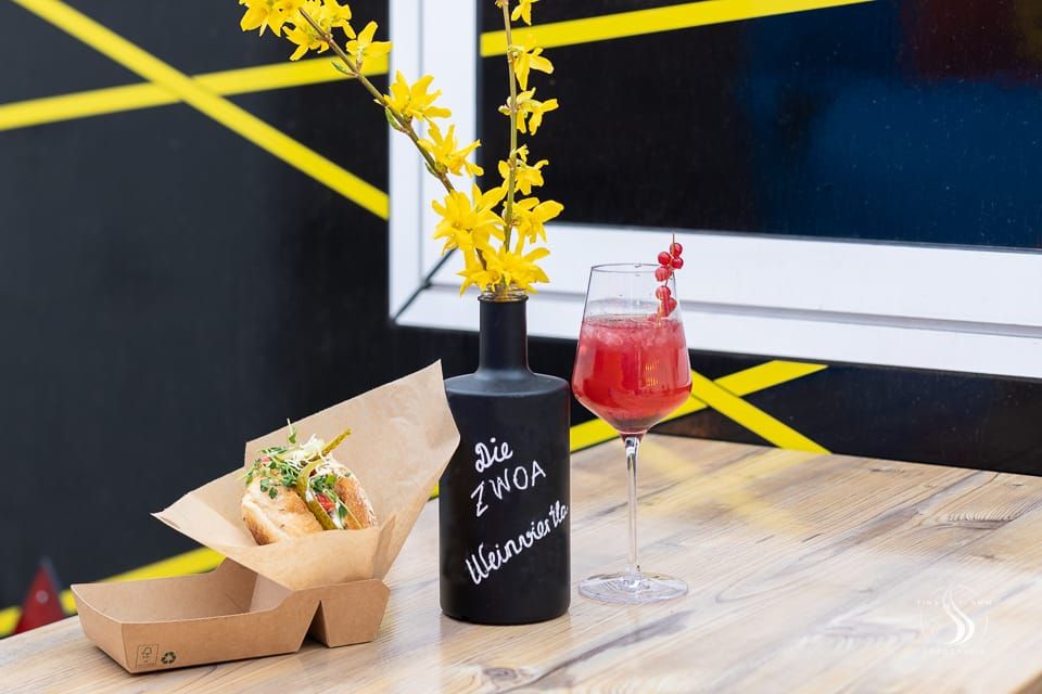 Nápoj a sendvič na stole s vázou se žlutými květy.