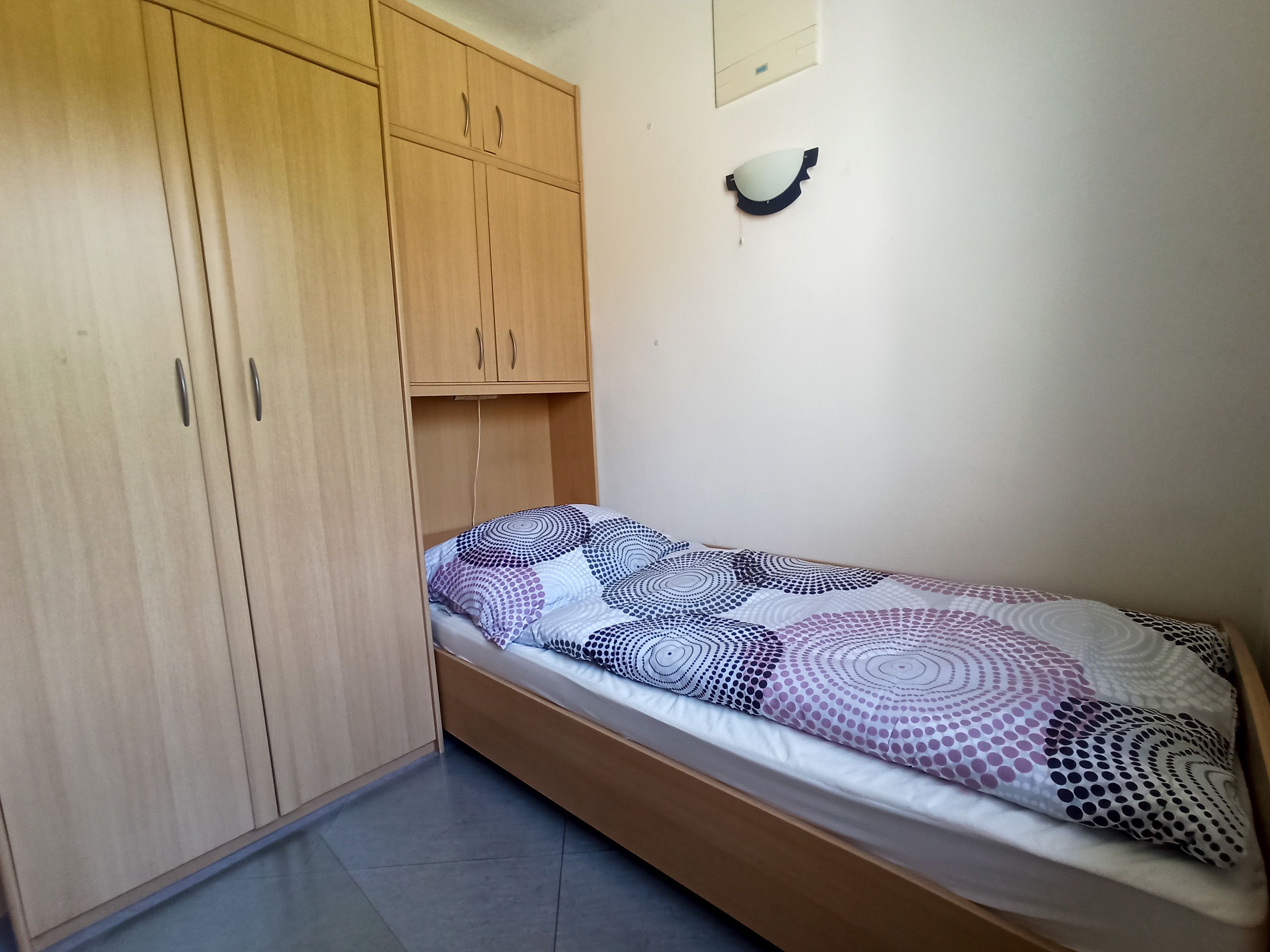 Jednoduchá ložnice s jednolůžkem a velkou dřevěnou skříní.