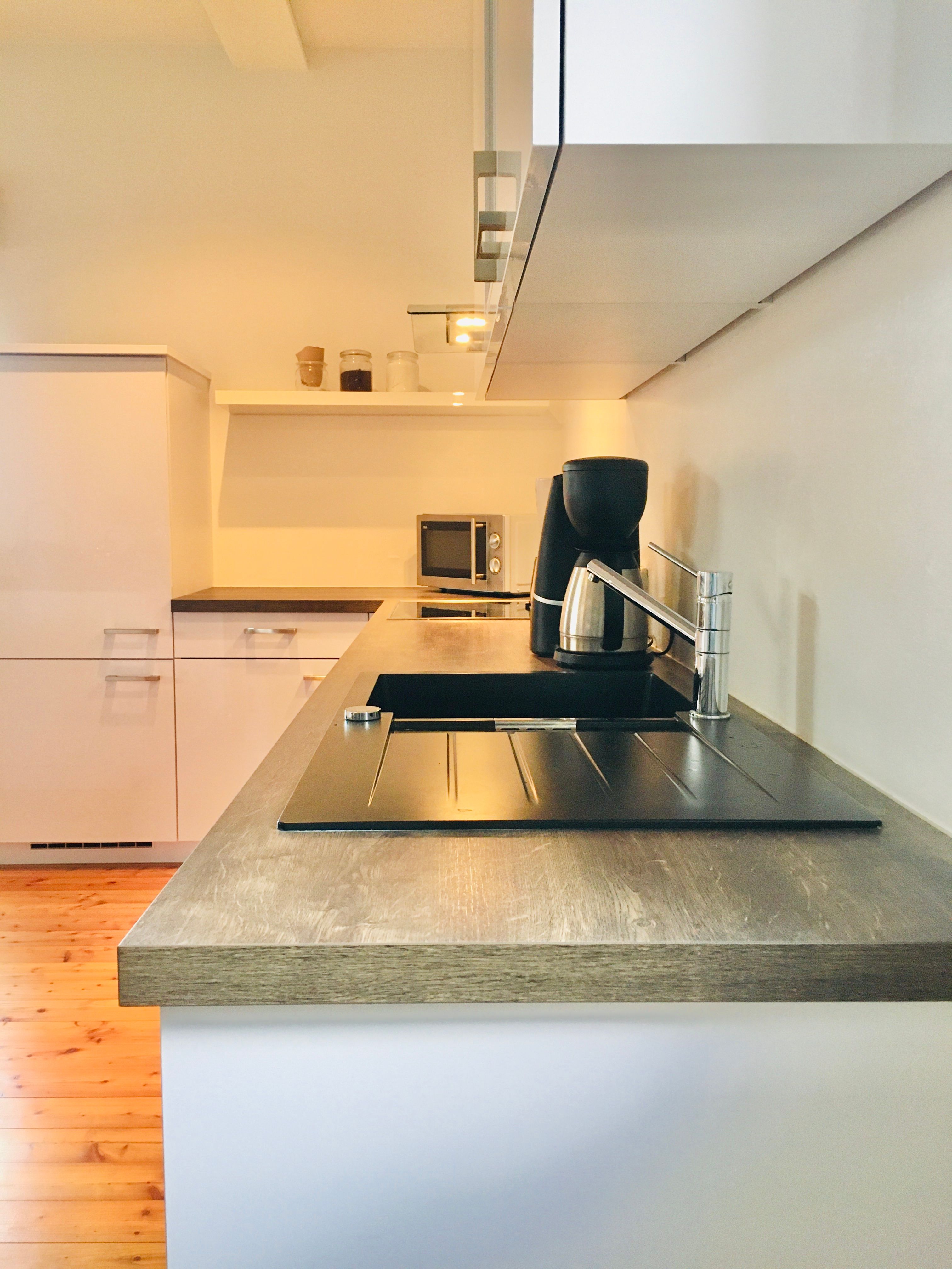 Moderní kuchyně s dřevěnou pracovní deskou, dřezem, kávovarem a mikrovlnnou troubou.