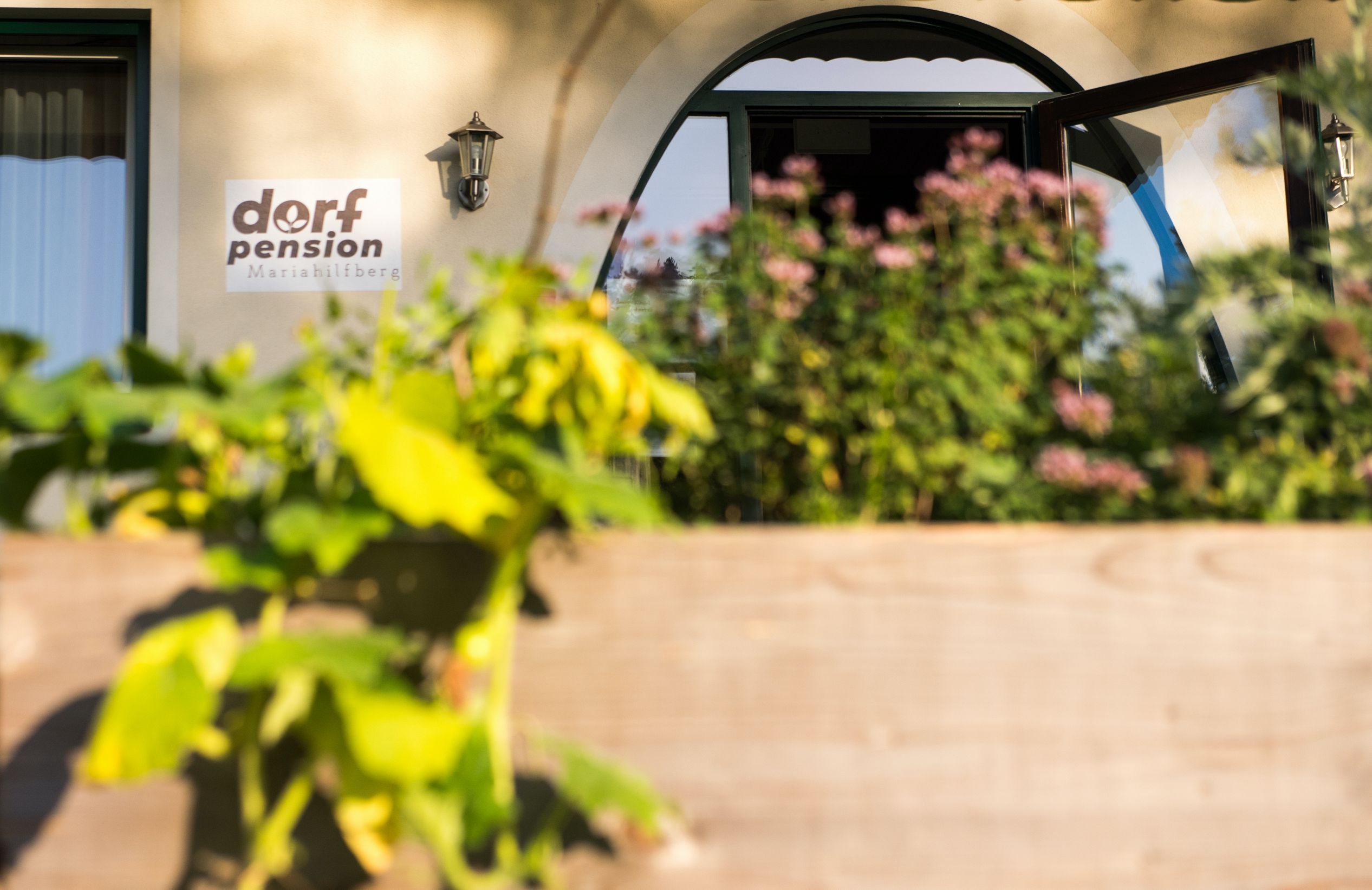 Vchod do vesnického penzionu Mariahilfberg s rostlinami v popředí.