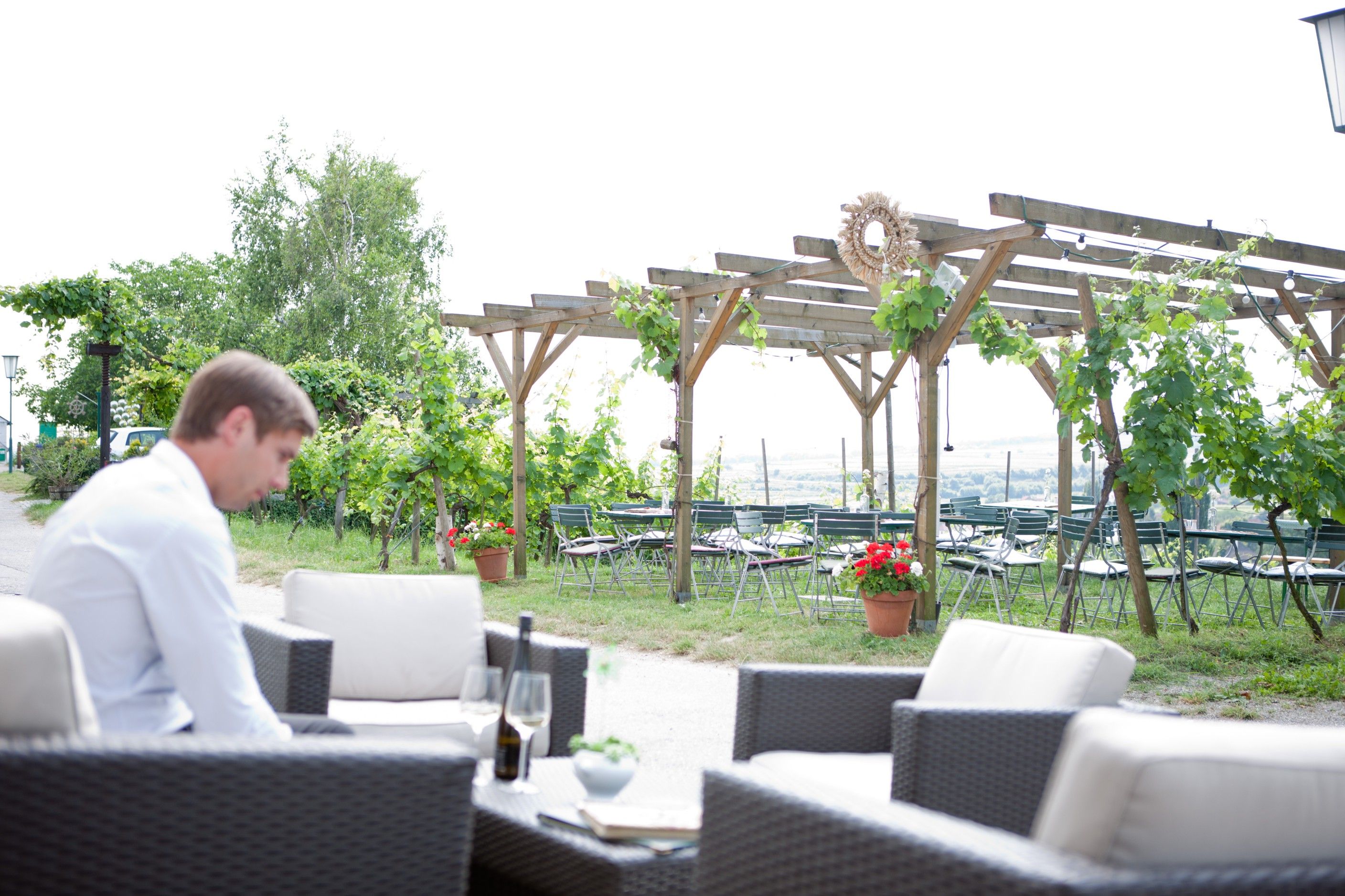 Muž sedí na zahrádce restaurace s vinnou révou a prázdnými stoly v pozadí.