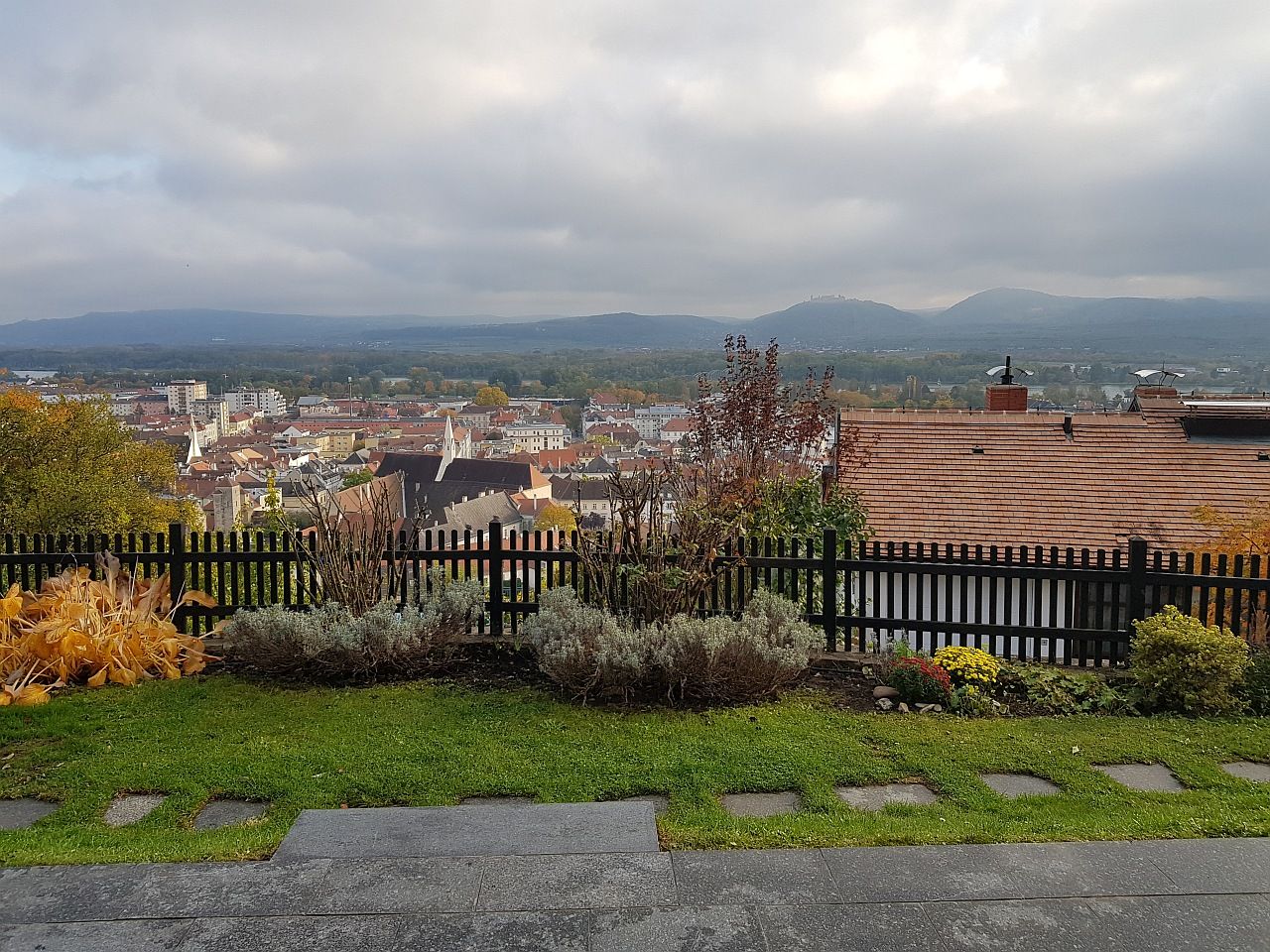 Pohled na město Krems s domy, kopci a zataženou oblohou v pozadí.