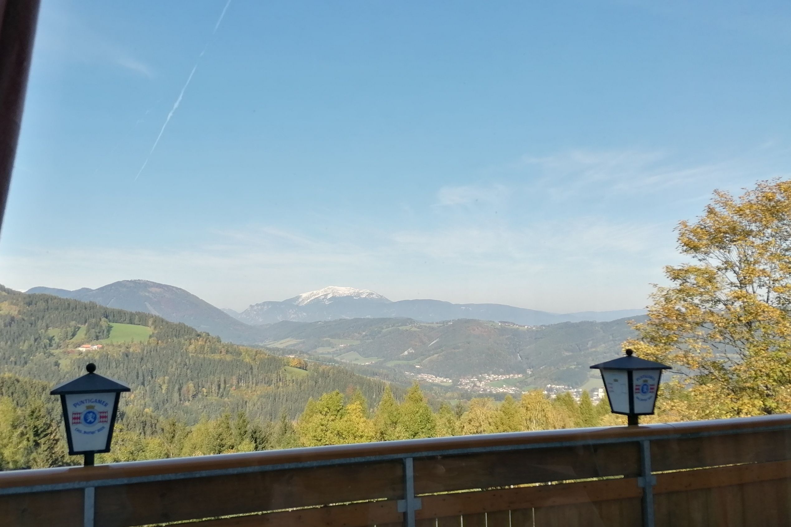 Pohled z balkonu restaurace na horskou krajinu s lesem a zasněženým vrcholem v pozadí.