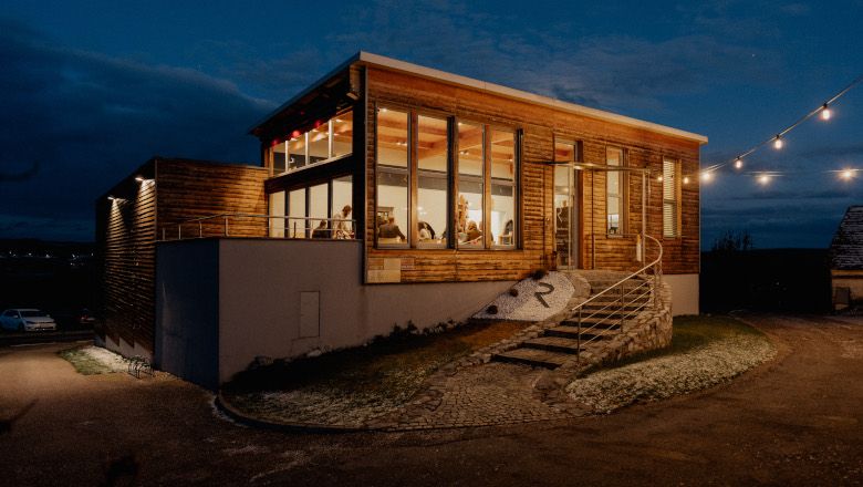 Pohled na moderní vinárnu v noci s osvětlenými okny a pohádkovými světly.