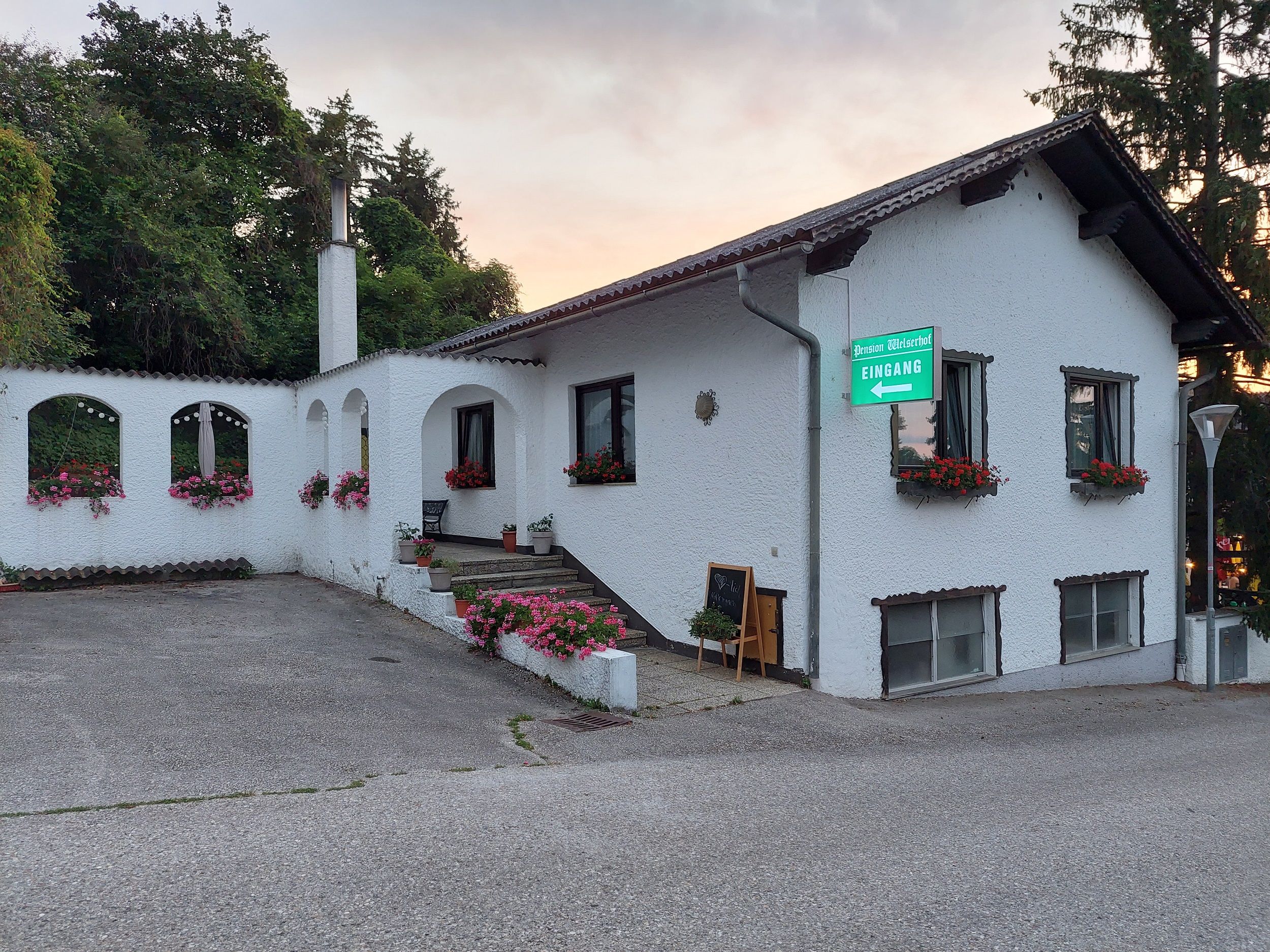 Pohled zvenčí na bílou budovu s květinami a nápisem "Pension Welserhof Eingang".