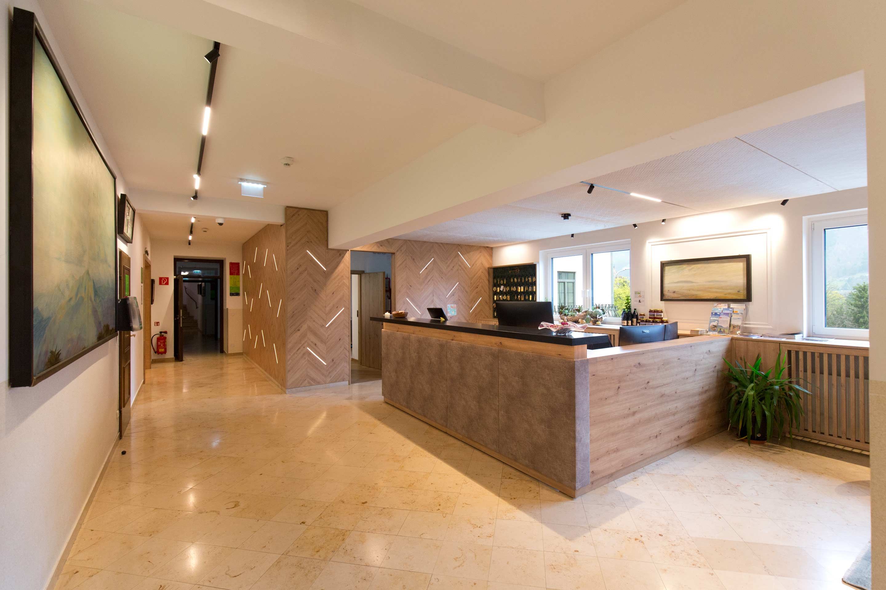 Recepce hotelu s moderním designem, dřevěnými prvky a velkým recepčním pultem.