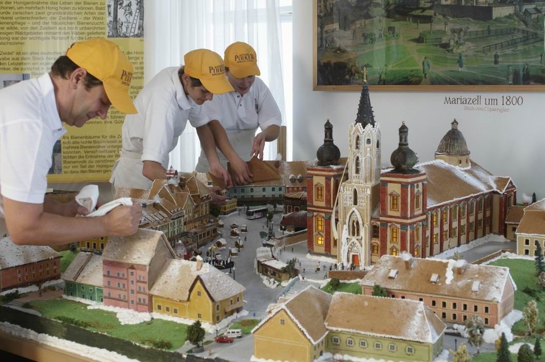 Tři lidé zdobí perníkový model Mariazell kolem roku 1800.