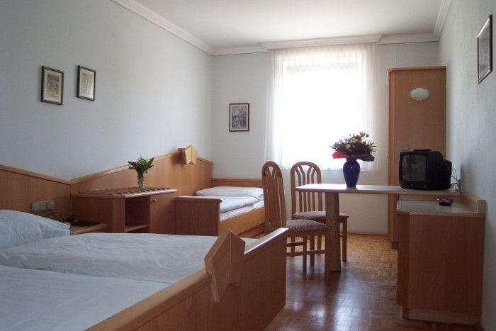 Jednoduše zařízený hotelový pokoj se dvěma lůžky, stolem, židlemi a malou televizí.