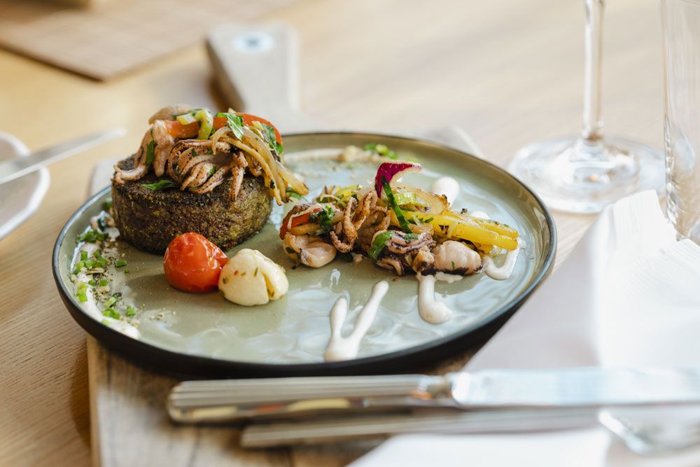 Gurmánský pokrm na talíři se zeleninou a mořskými plody, ozdobně naaranžovaný.