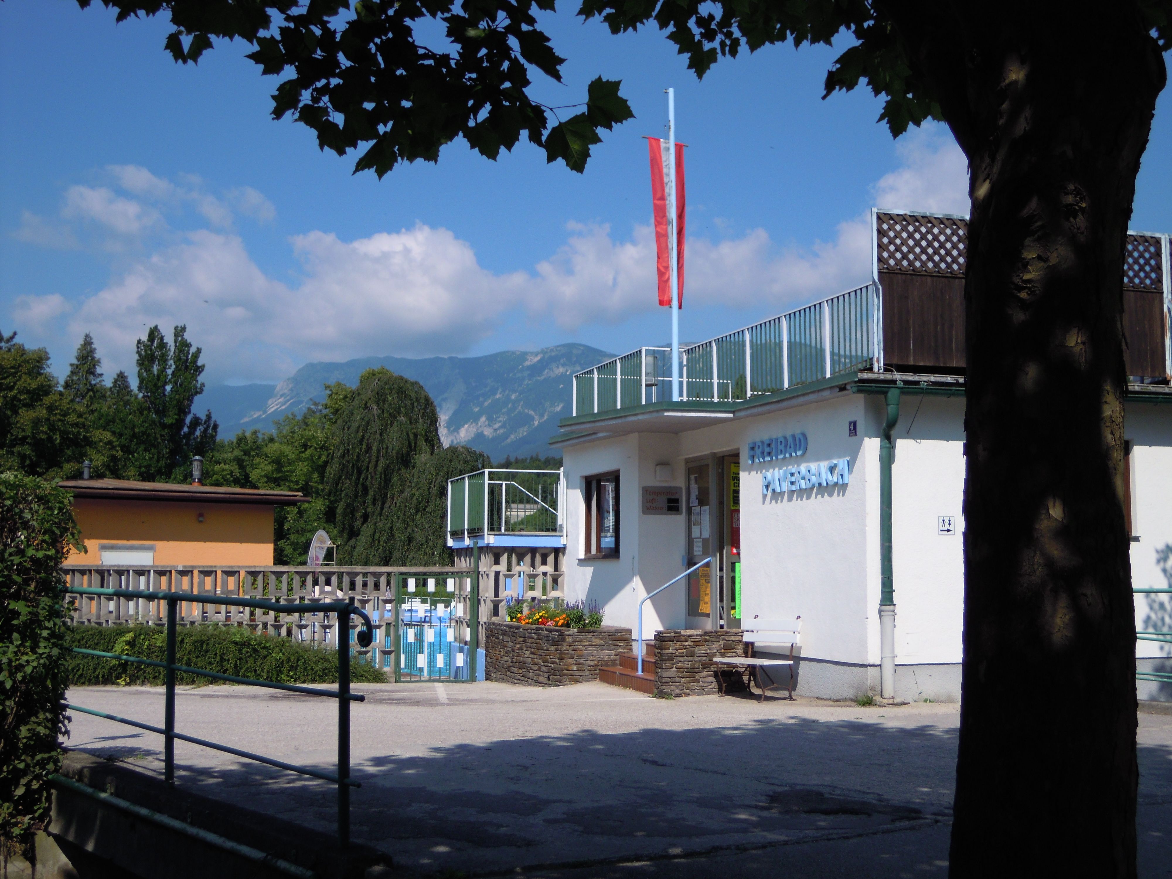 Vstup do venkovního bazénu Payerbach s horskou krajinou v pozadí.