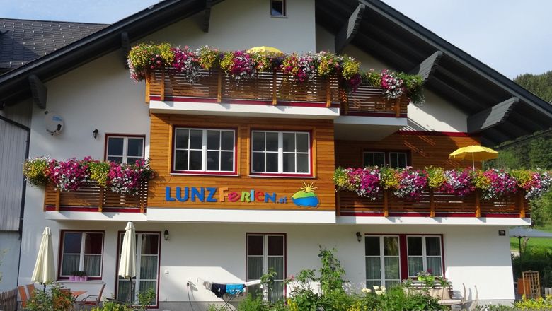 Rekreační dům s barevnými květinami na balkonech a nápisem "LUNZ Ferien".