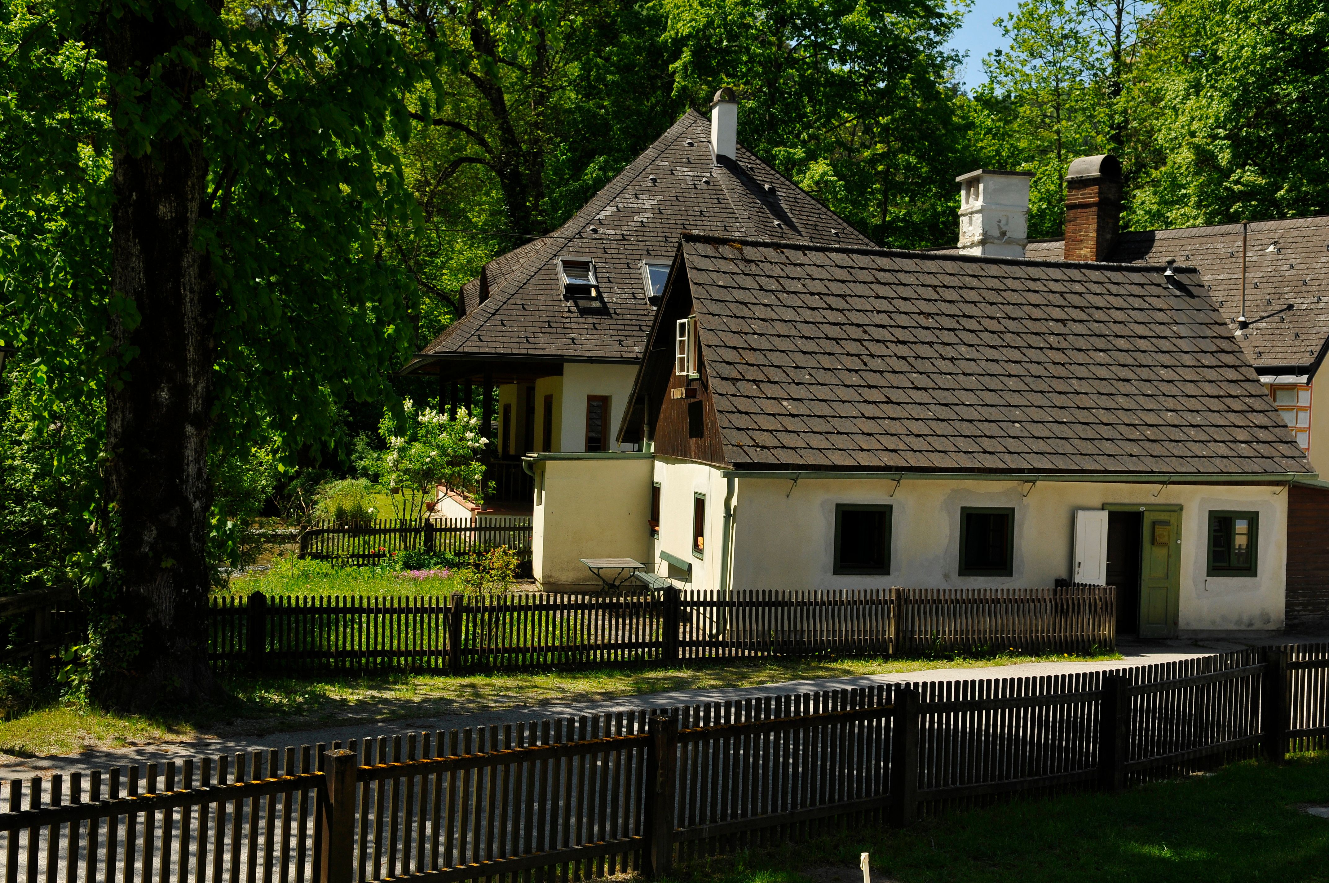 Tradiční penzion s dřevěným plotem a zahradou obklopenou stromy.