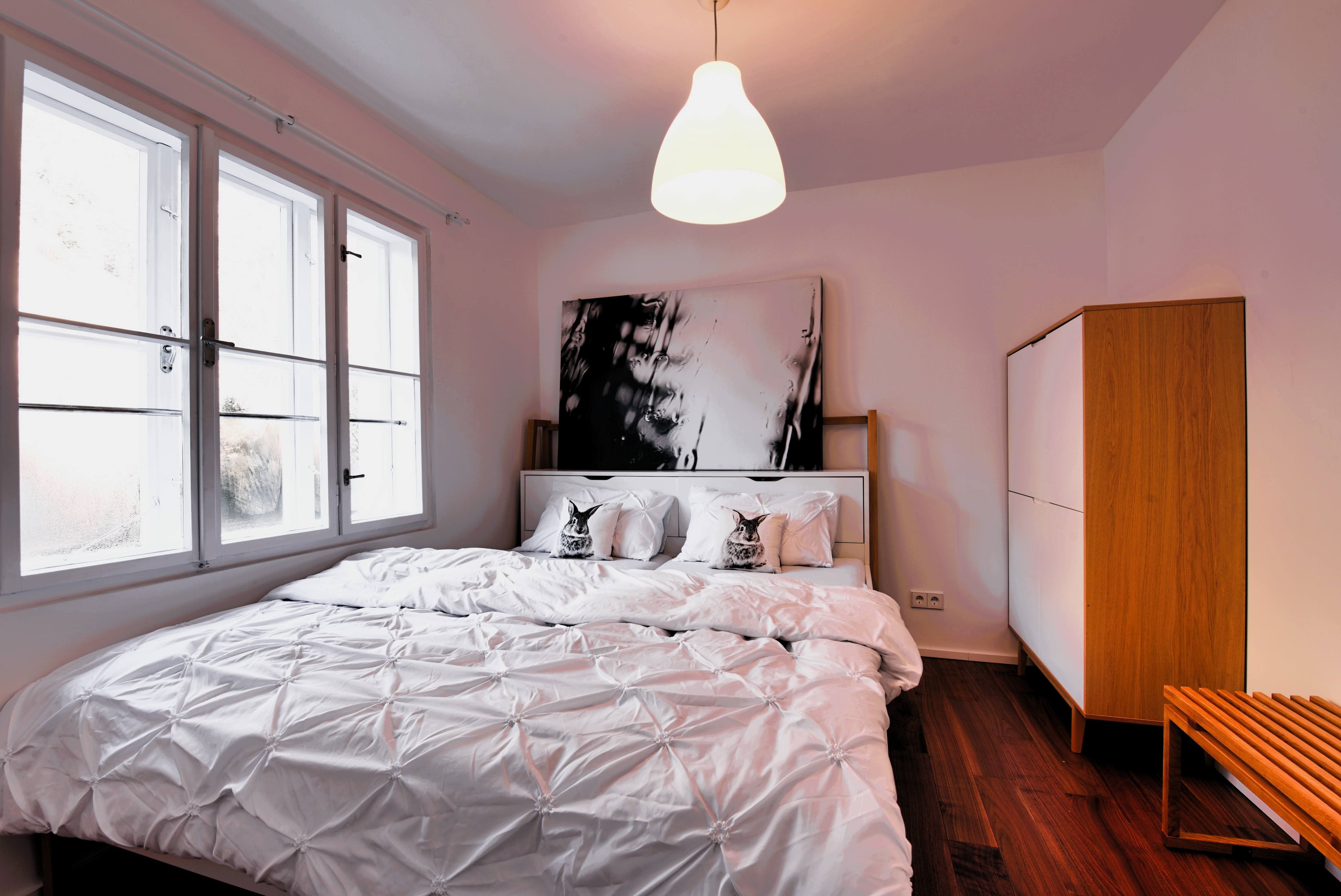 Moderní ložnice s velkou postelí, bílým ložním prádlem a dřevěnou skříní.