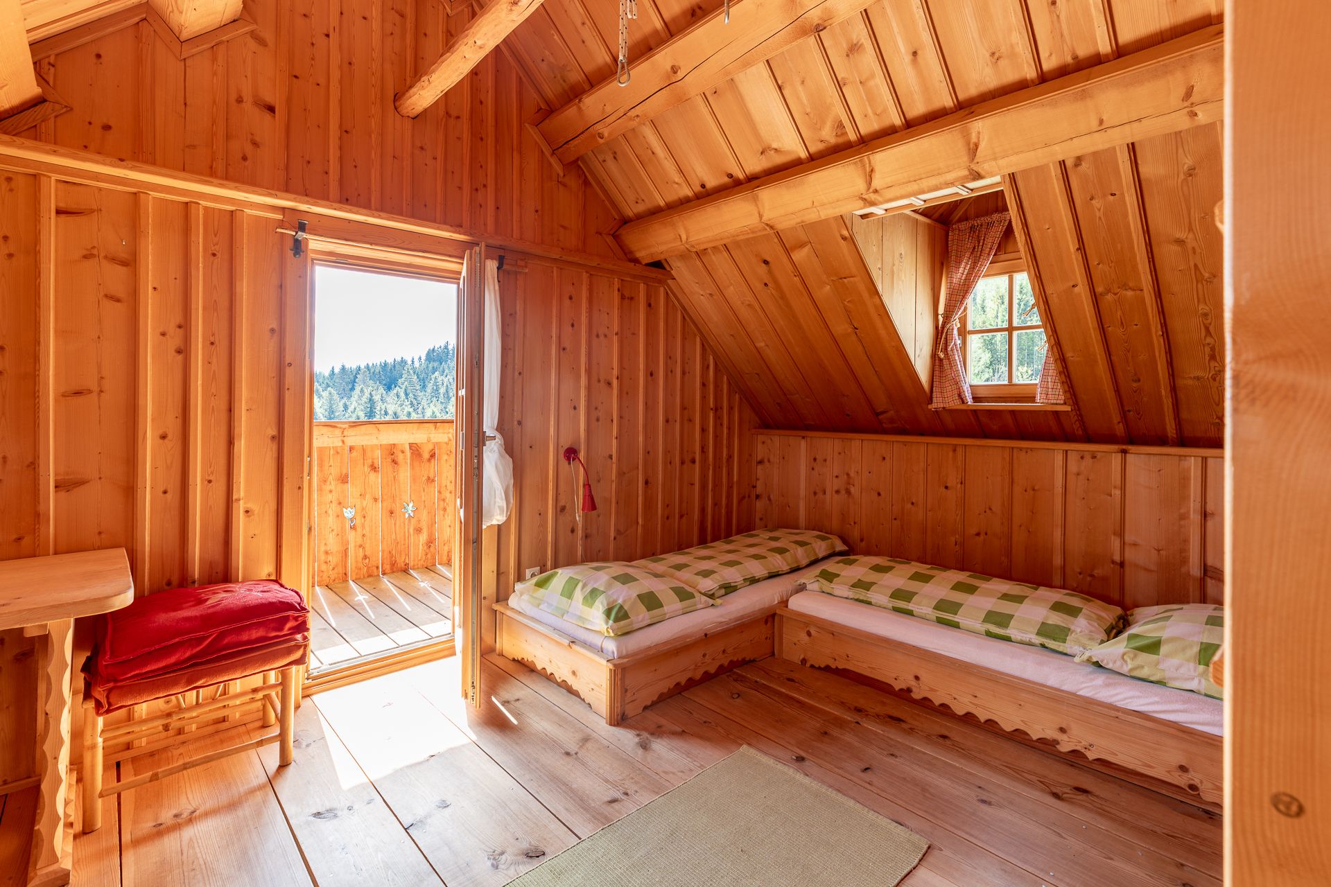 Ložnice s dřevěným obložením, dvěma lůžky, oknem a otevřenými dveřmi na balkon.