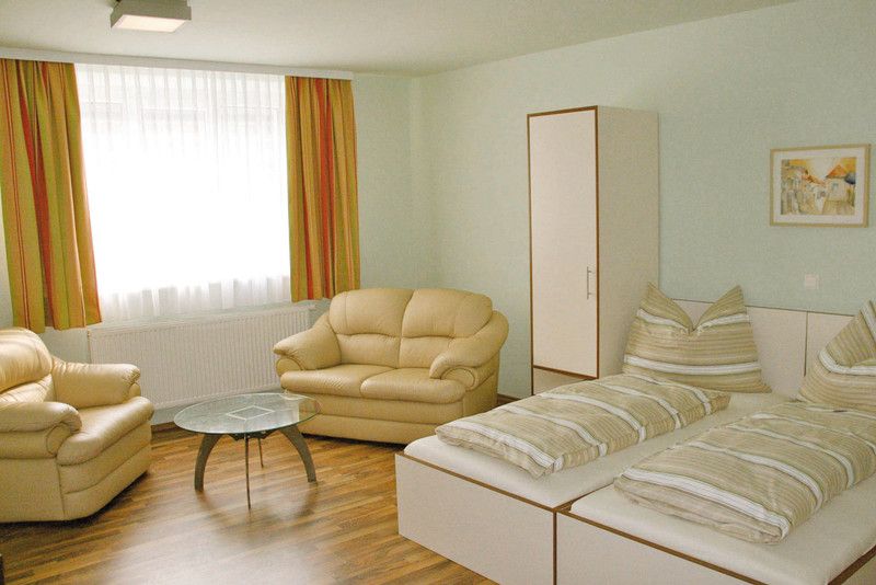 Světlý pokoj se dvěma lůžky, pohovkami, stolem a šatní skříní.