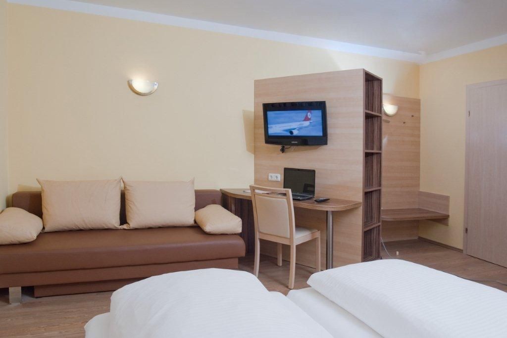 Hotelový pokoj s pohovkou, psacím stolem, televizí a postelí.