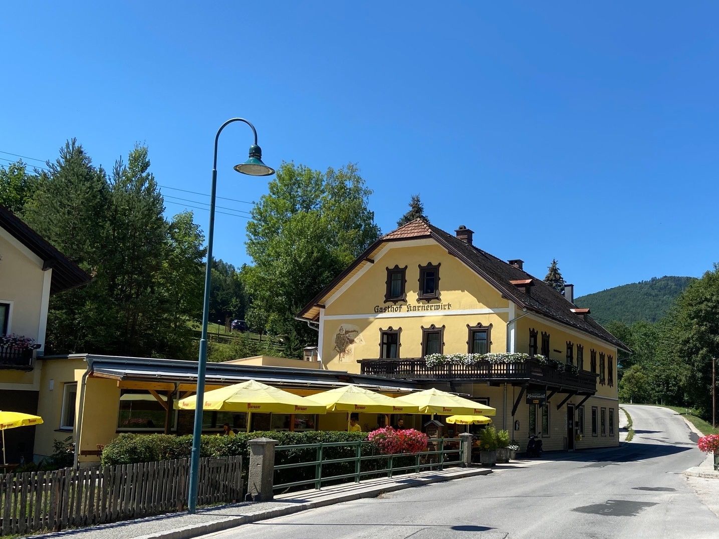 Žlutý hostinec s balkonem a slunečníky na pozadí modré oblohy.