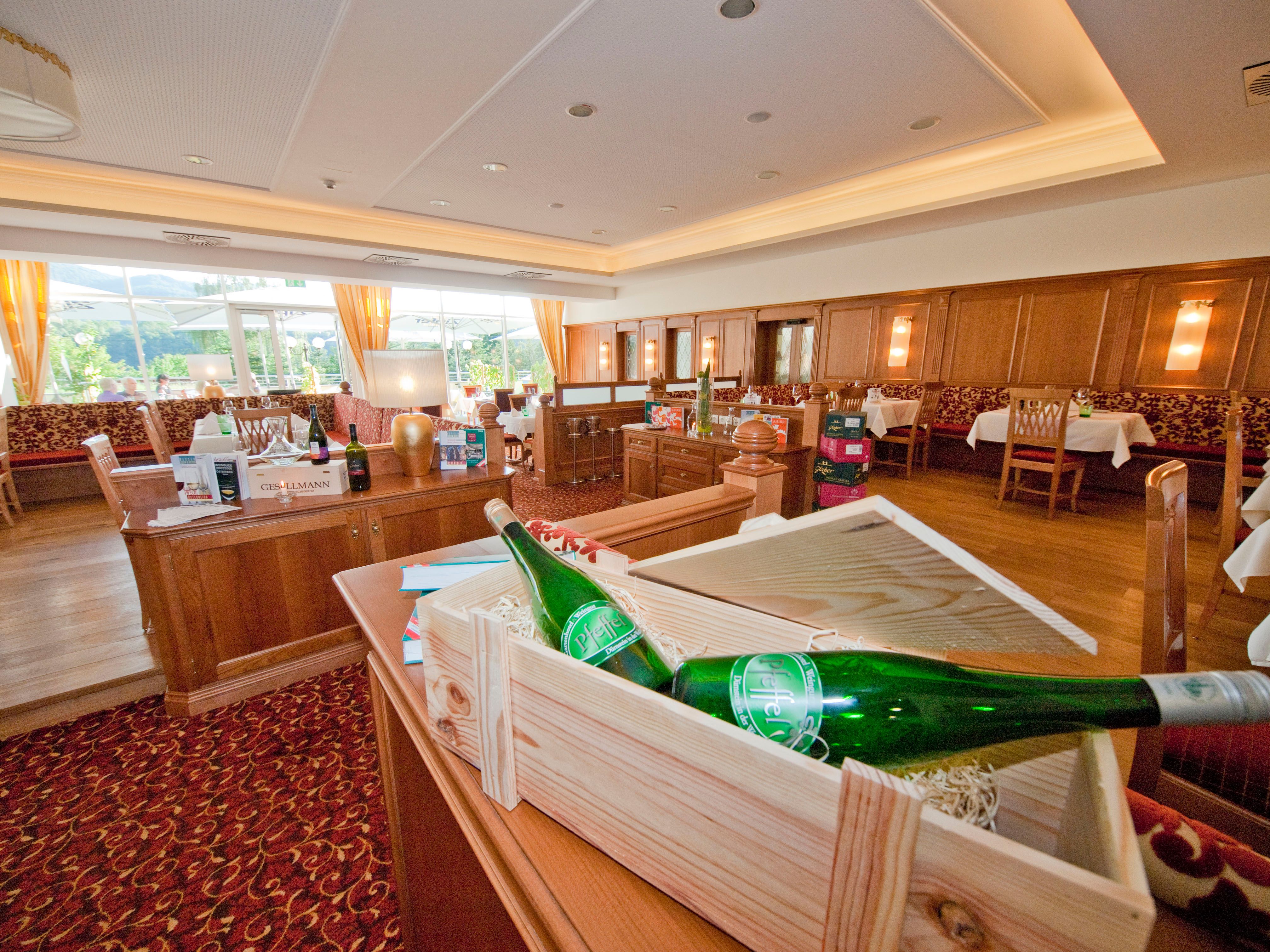 Pohled do interiéru elegantní restaurace s dřevěným nábytkem a lahvemi vína.