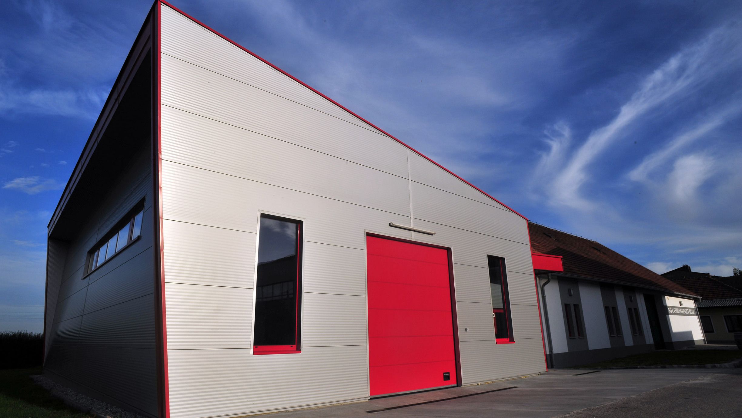 Moderní budova s červenou bránou a modrou oblohou v pozadí.