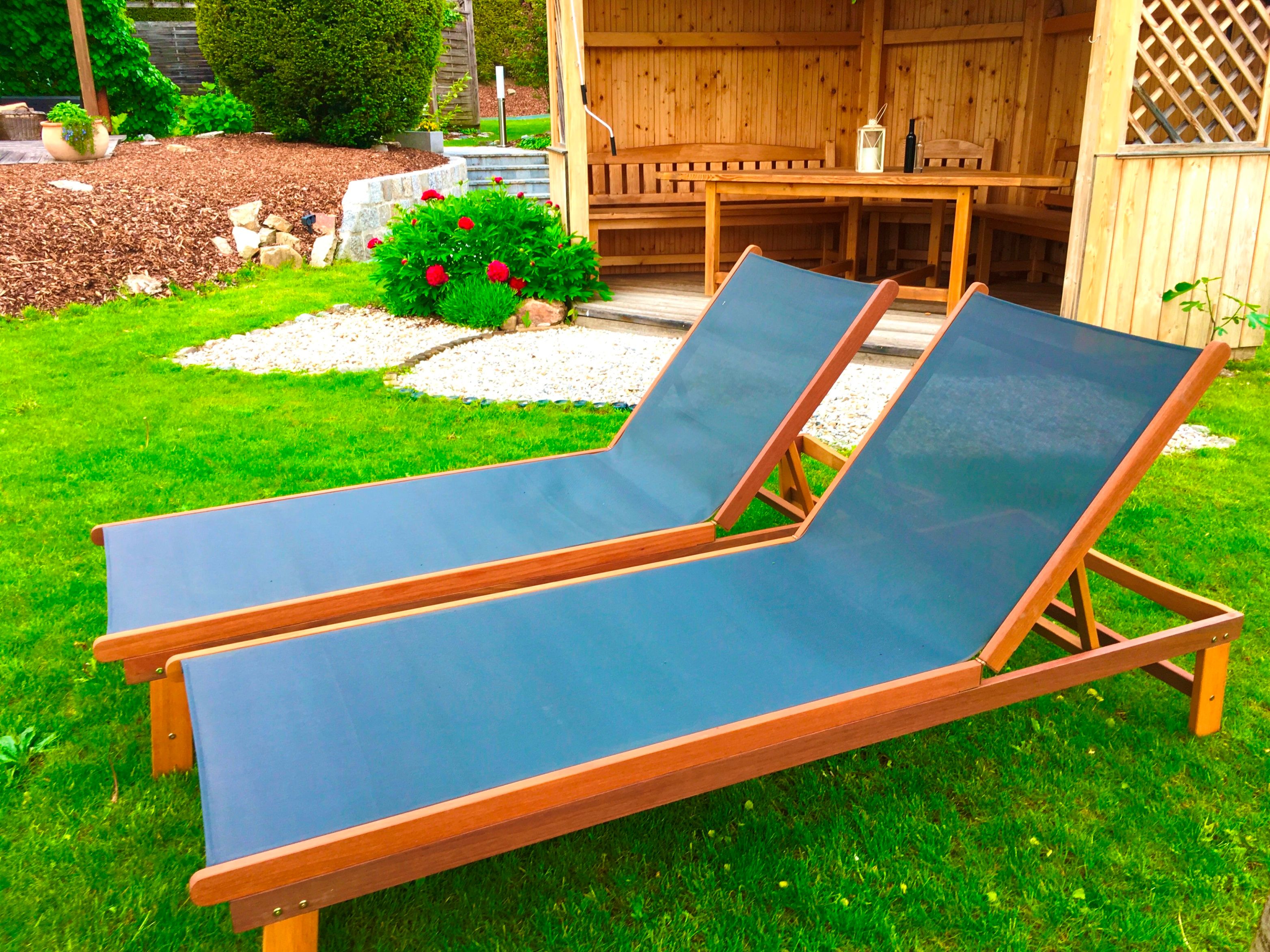 Dvě modrá lehátka na zeleném trávníku před dřevěnou chatkou v zahradě.