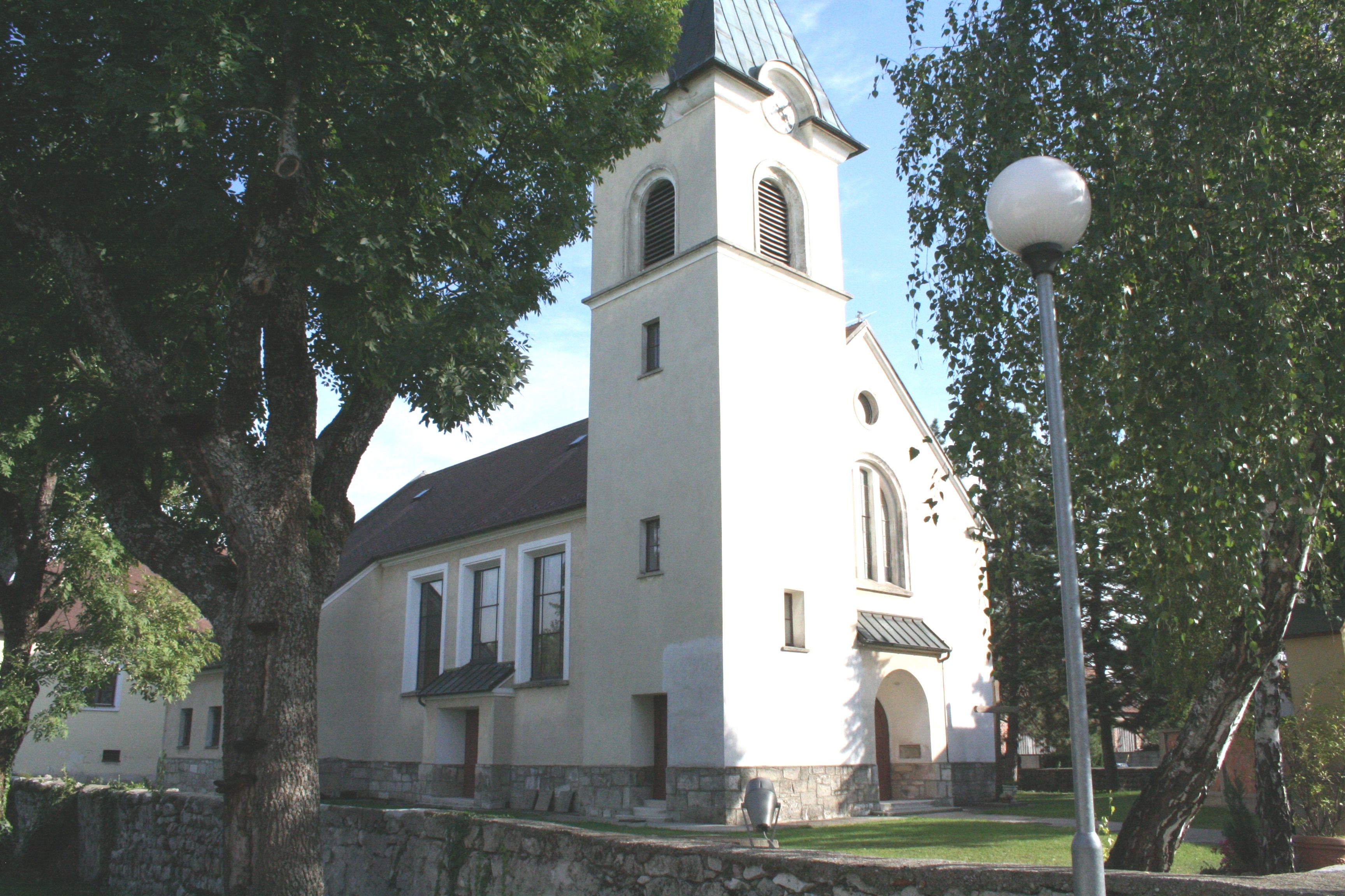 Kostel v Pischelsdorfu s věží a stromy v popředí.