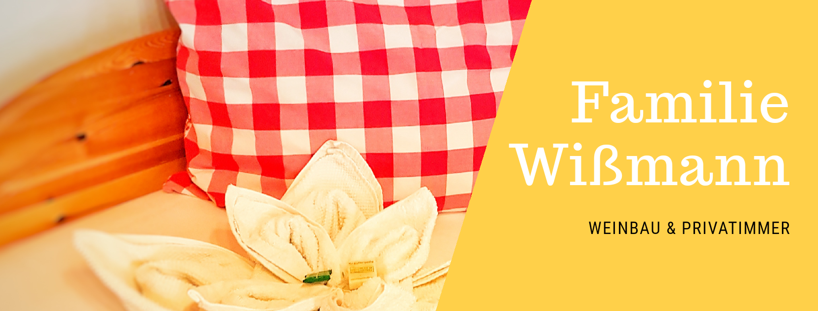 Červený polštář s kostkovaným vzorem a ručník ve tvaru květiny na posteli. Text: Wißmann, vinařství a soukromé pokoje.