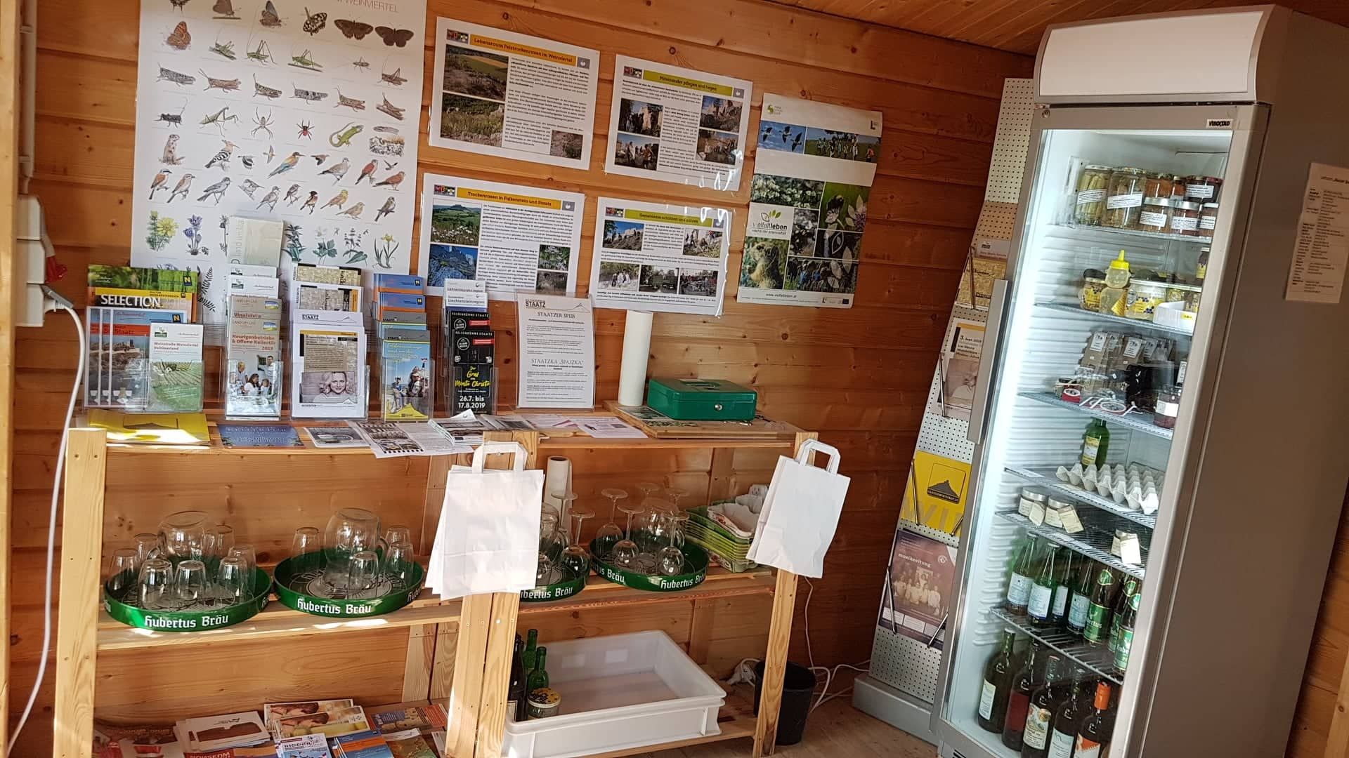 Pohled do interiéru malého prodejního stánku s informačními materiály a lednicí.