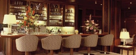 Elegantní bar s dřevěným obložením, květinovou výzdobou a čalouněnými barovými stoličkami.