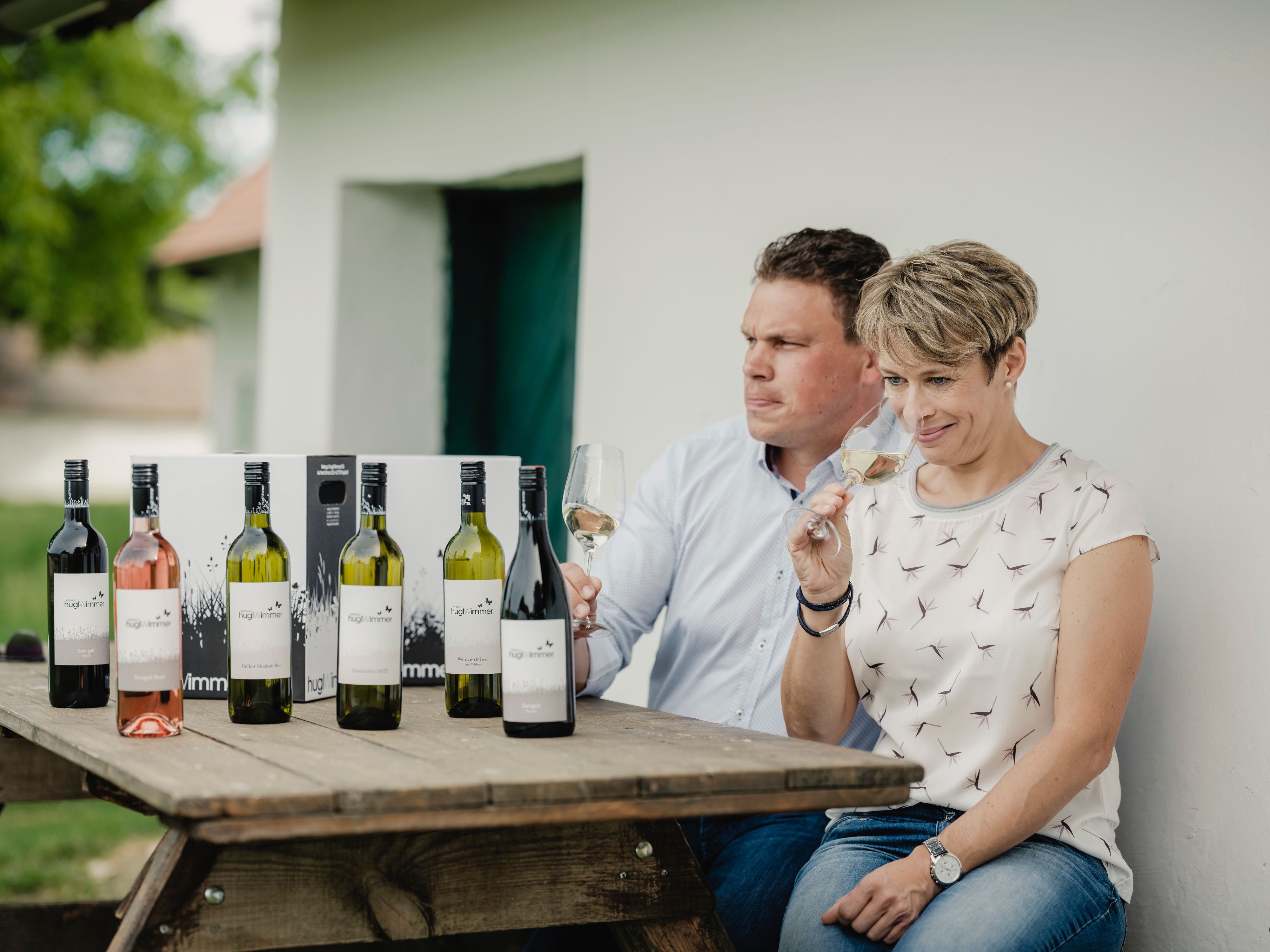 Dva lidé sedí u stolu s lahvemi vína a ochutnávají víno.