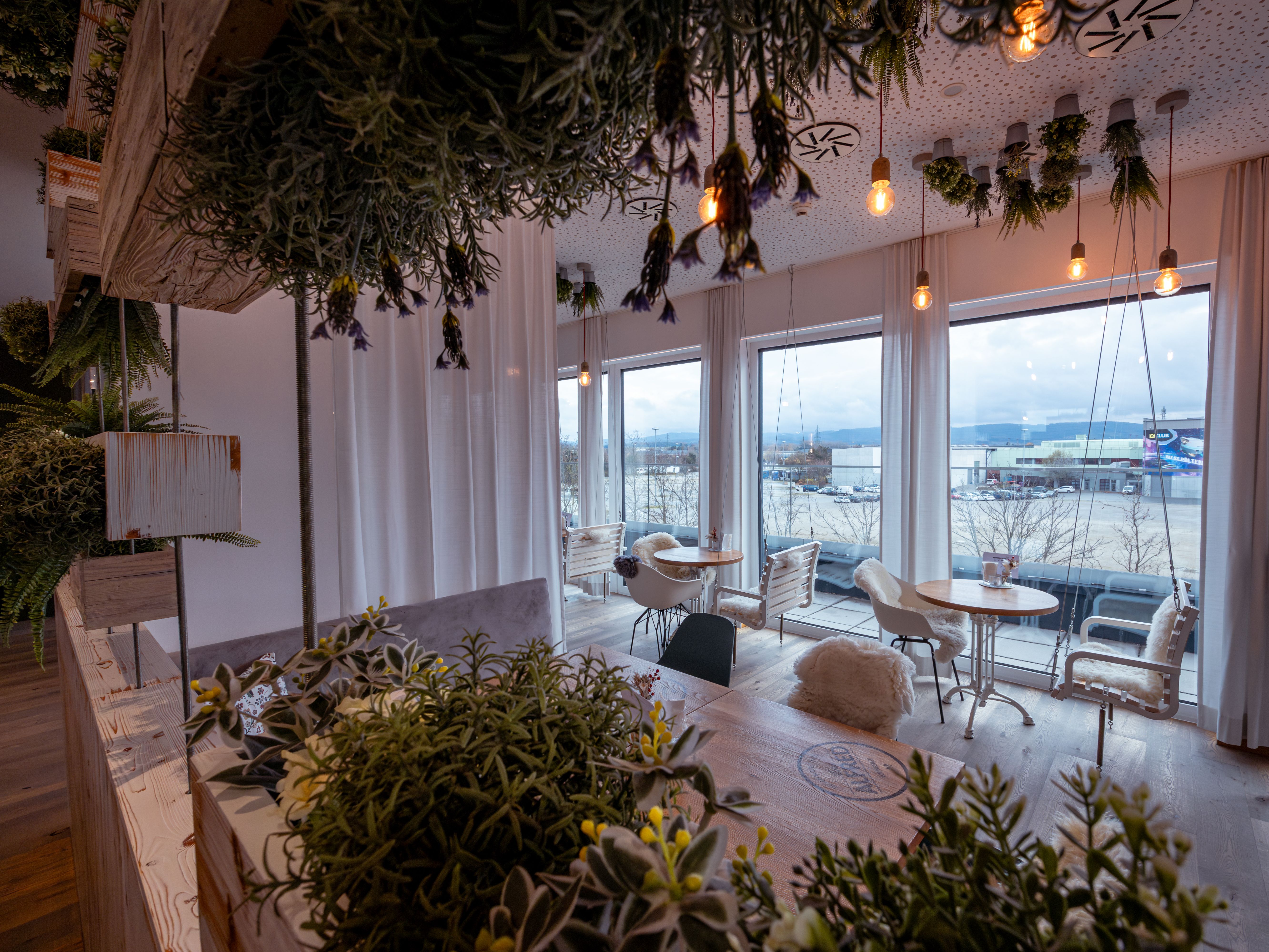 Moderní hotelový pokoj s manželskou postelí, dřevěným obložením a okny se závěsy.