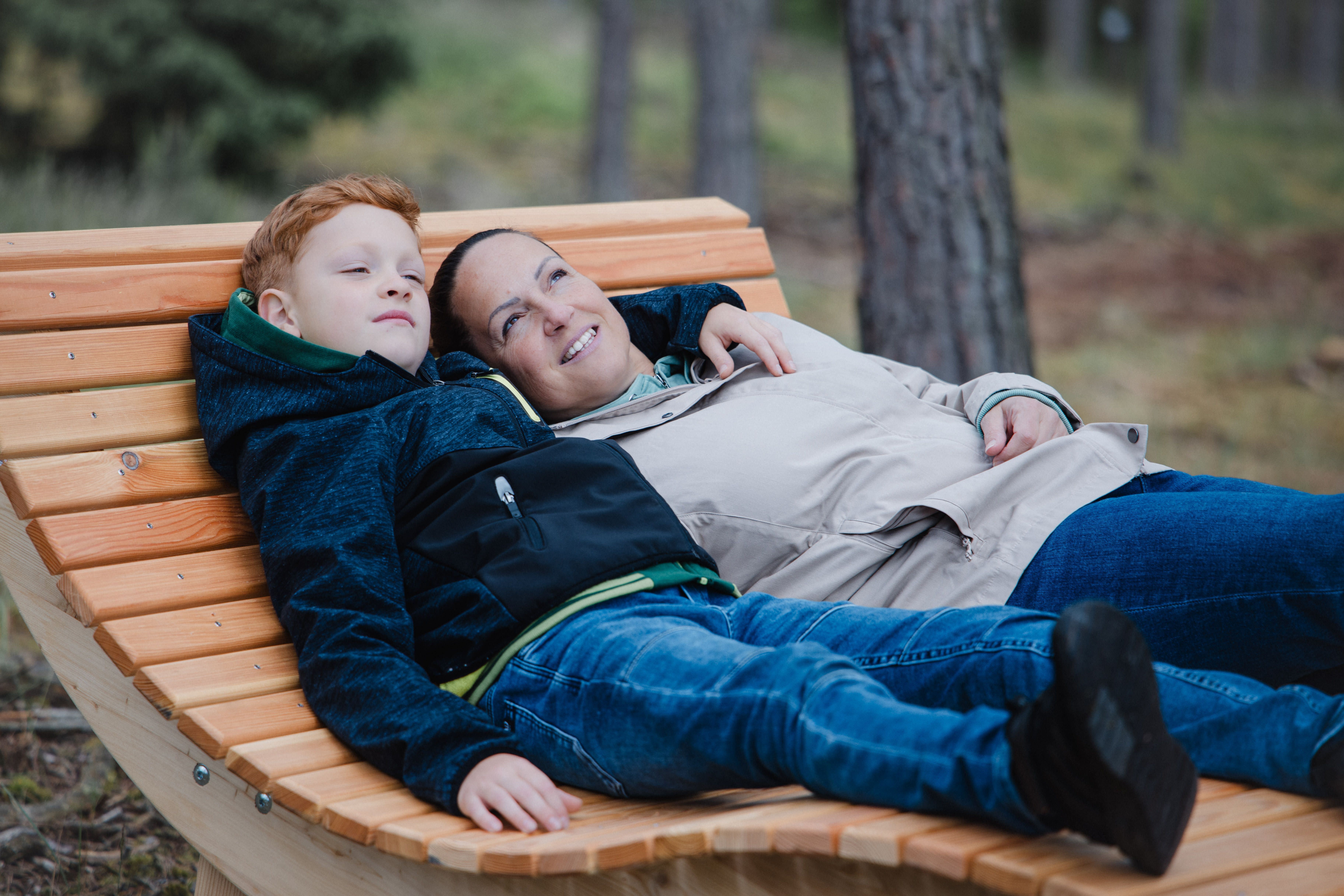 Dva lidé odpočívají na dřevěné lavičce v lese.