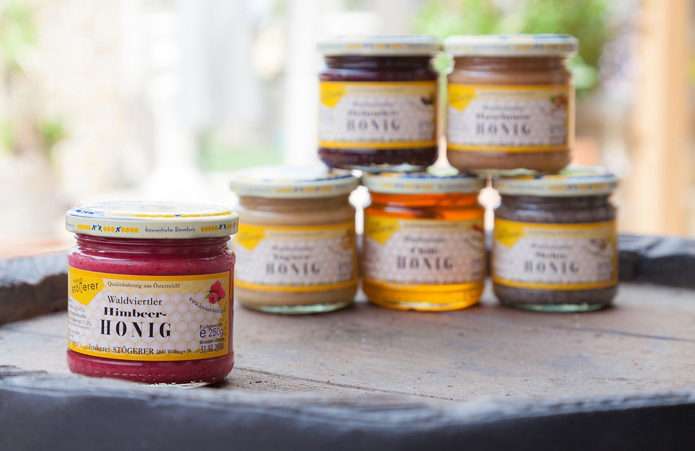 Různé sklenice s medem na stole, v popředí malinový med.