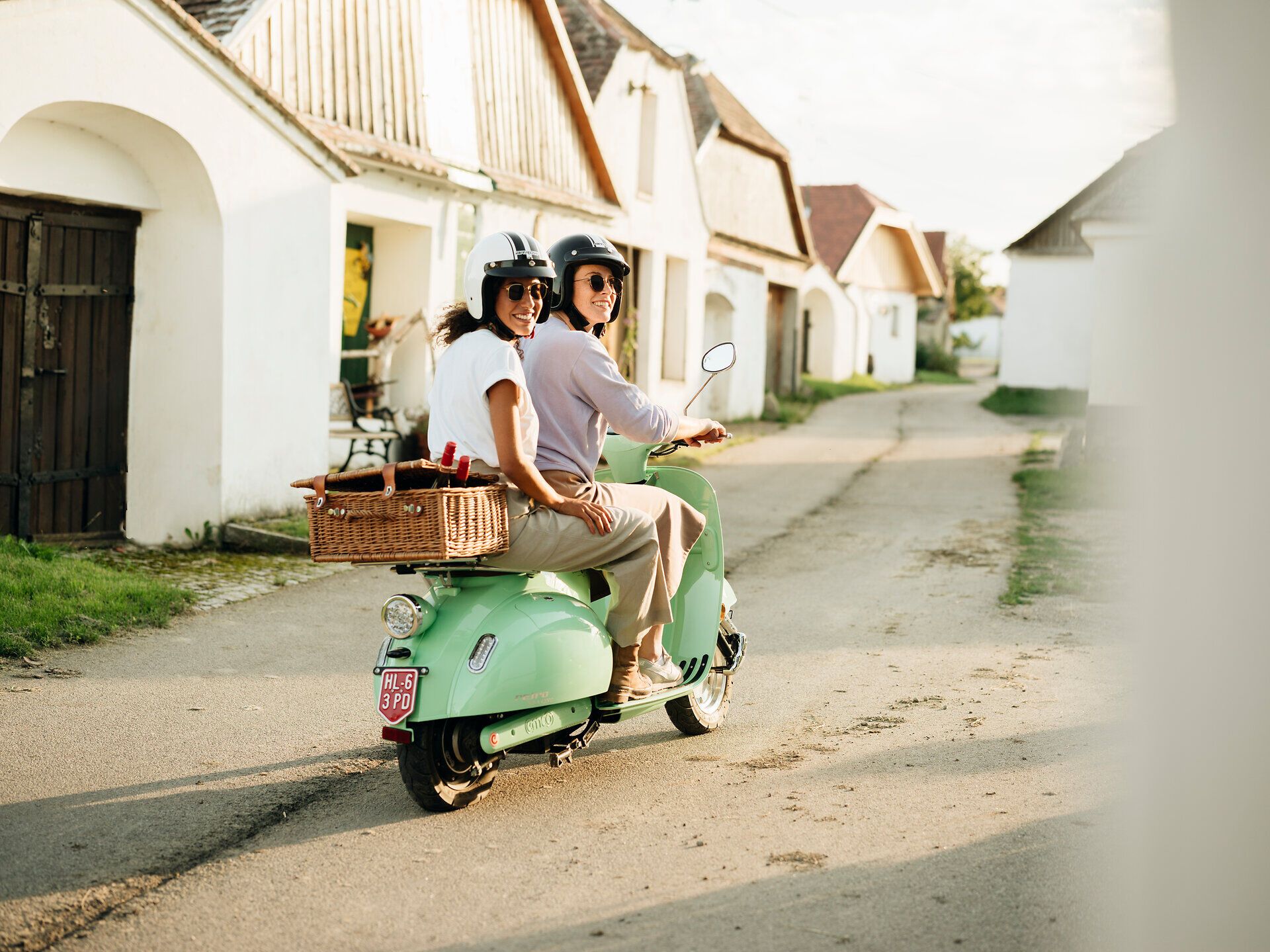 Ein fröhliches Paar genießt die sanfte Brise des Herbstes auf ihrem Roller, während sie durch die malerischen Gassen der Kellergasse Maulavern fahren. Umgeben von idyllischen Weinhängen und charmanten Weinkellern, strahlt die Szene eine entspannte Urlaubsatmosphäre aus, die zum Entdecken einlädt.