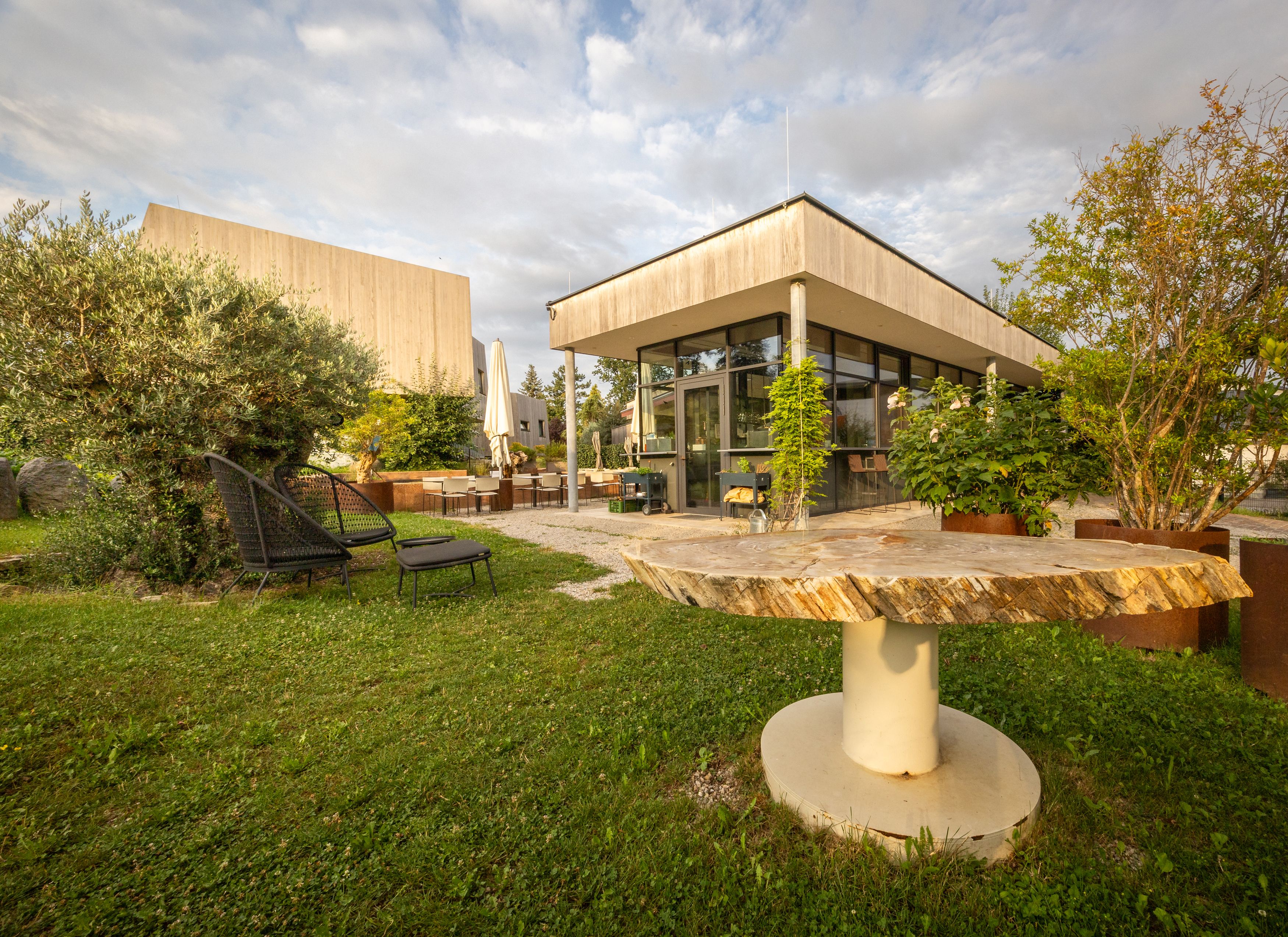 Zahrada moderního hotelu s posezením a rostlinami.