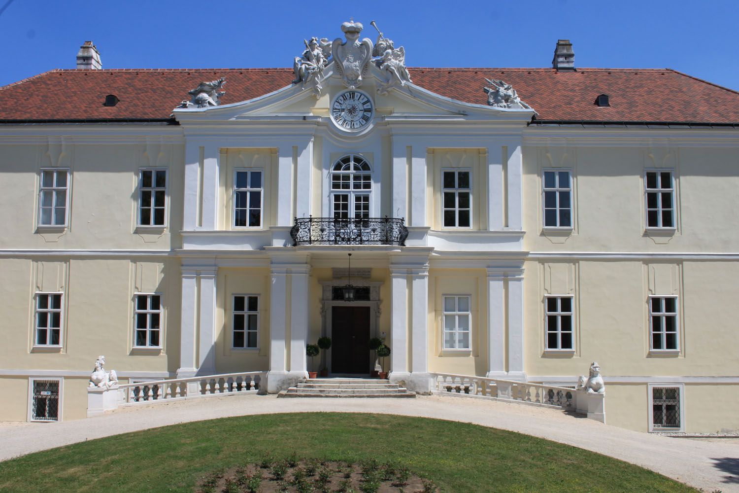 Pohled na Lichtenštejnský hrad s hodinami a sochami na střeše.