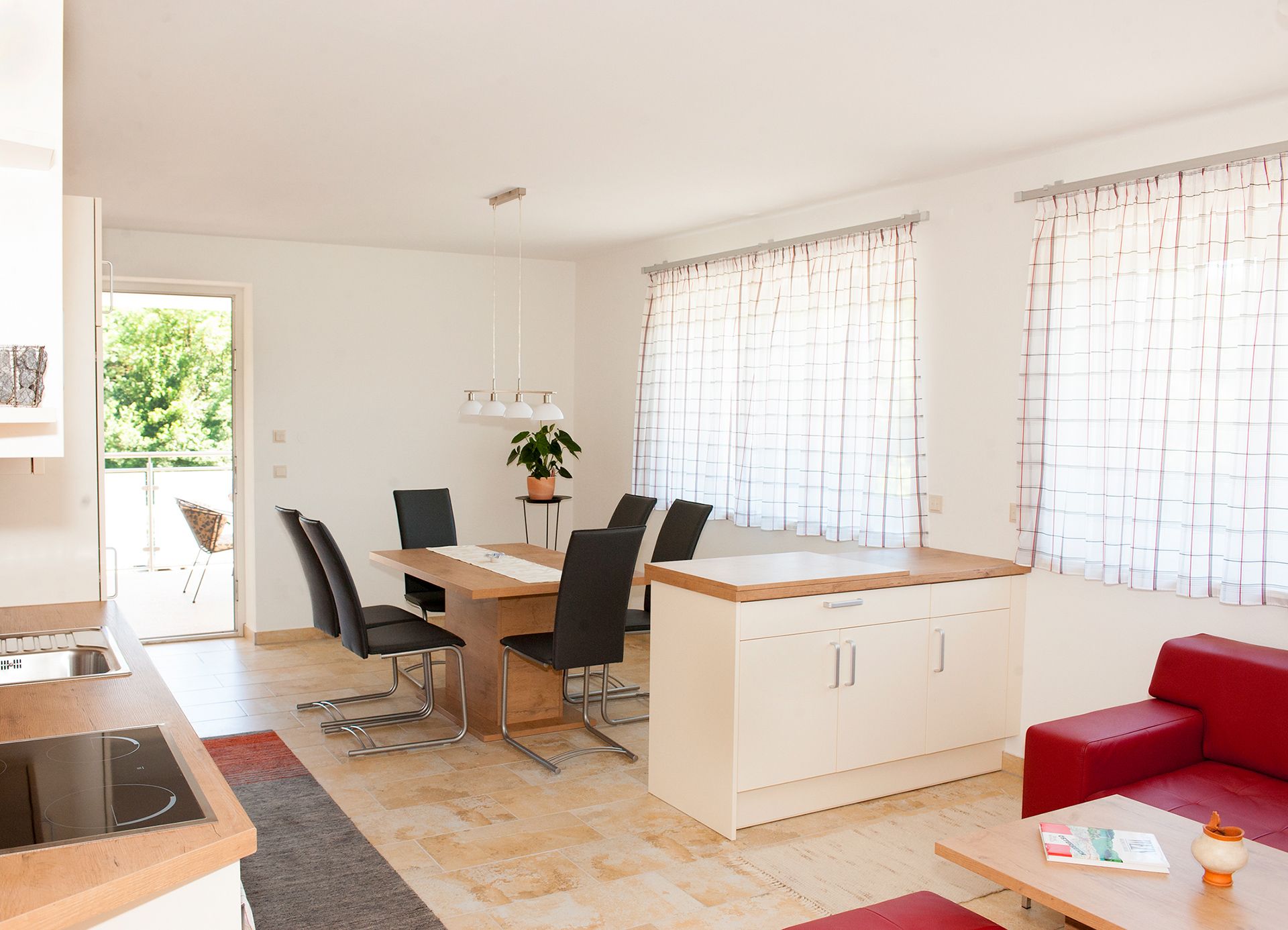 Moderní jídelní kout s dřevěným stolem, černými židlemi a velkými okny se závěsy.