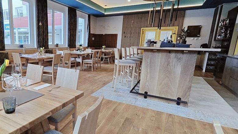 Bar a vstupní prostor moderní restaurace s dřevěným nábytkem a prostřenými stoly.