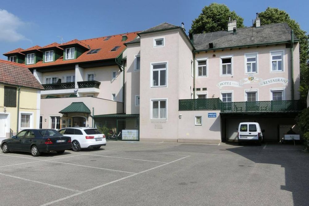 Pohled zvenčí na hotel s parkovištěm a auty.