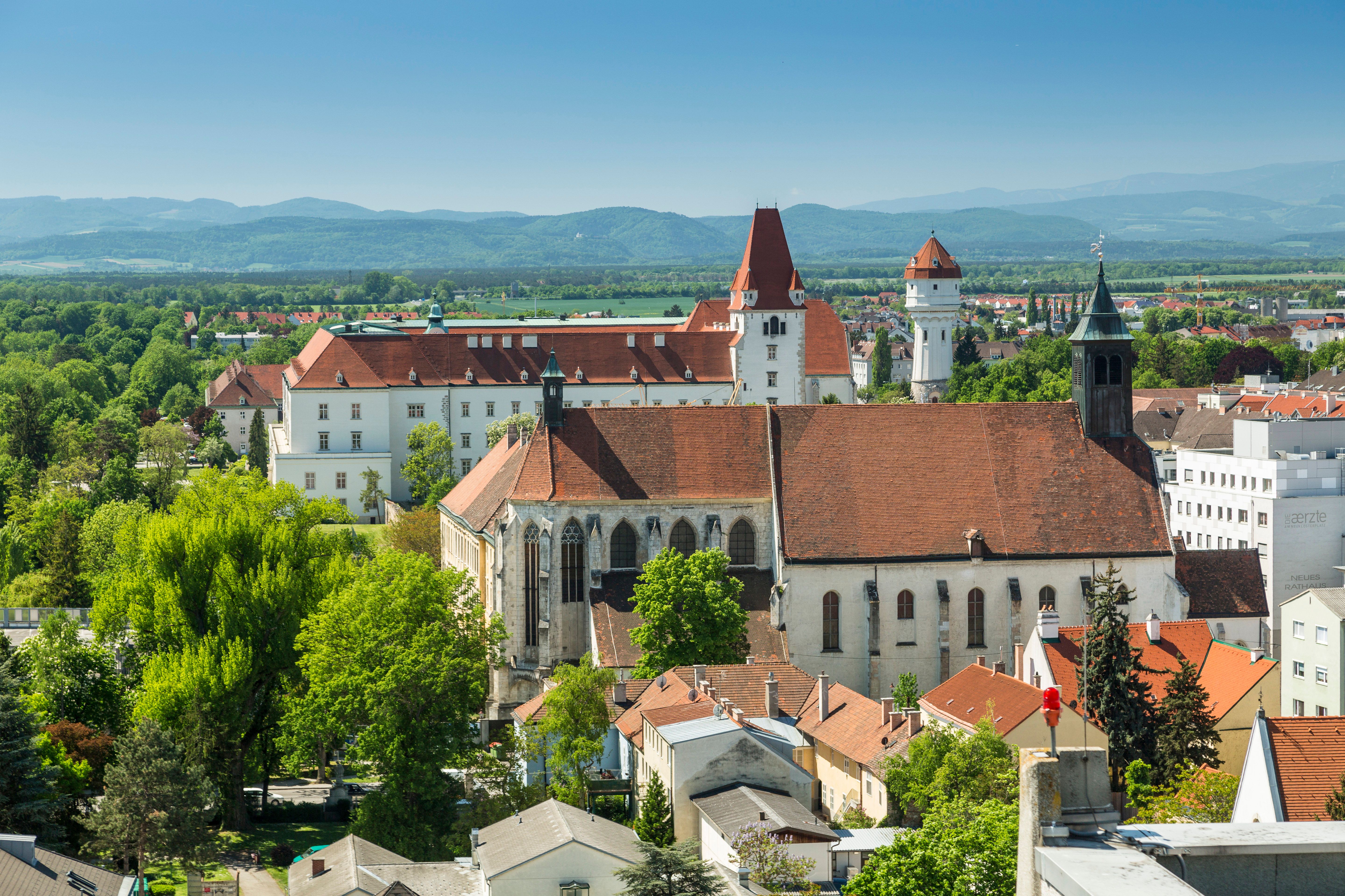 Tři památky na jedné fotografii: klášter Neukloster, Tereziánská vojenská akademie v Akademieparku a vodárenská věž. V pozadí jsou hory Vídeňských Alp.