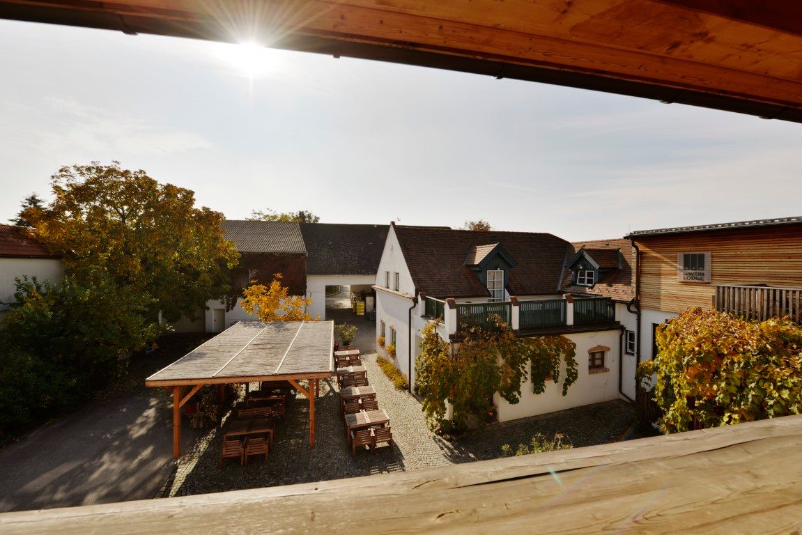 Nádvoří vinařství se stoly a židlemi pod dřevěným pavilonem, obklopené budovami a podzimním listím.