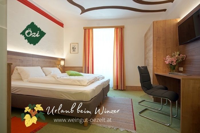 Útulný pokoj pro hosty s manželskou postelí, psacím stolem a židlí, vyzdobený květinami. Světlé závěsy a podlaha s kobercem.