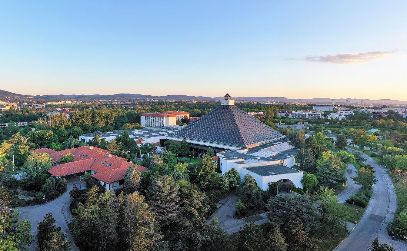 Letecký pohled na hotel Pyramida s okolní krajinou a budovami při západu slunce.