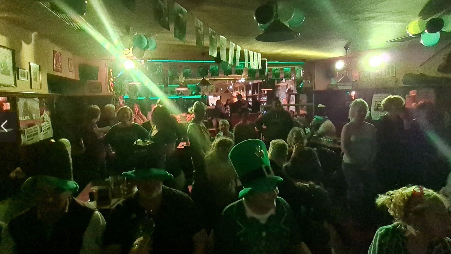 Lidé slaví Den svatého Patrika v hospodě se zelenými dekoracemi a klobouky.