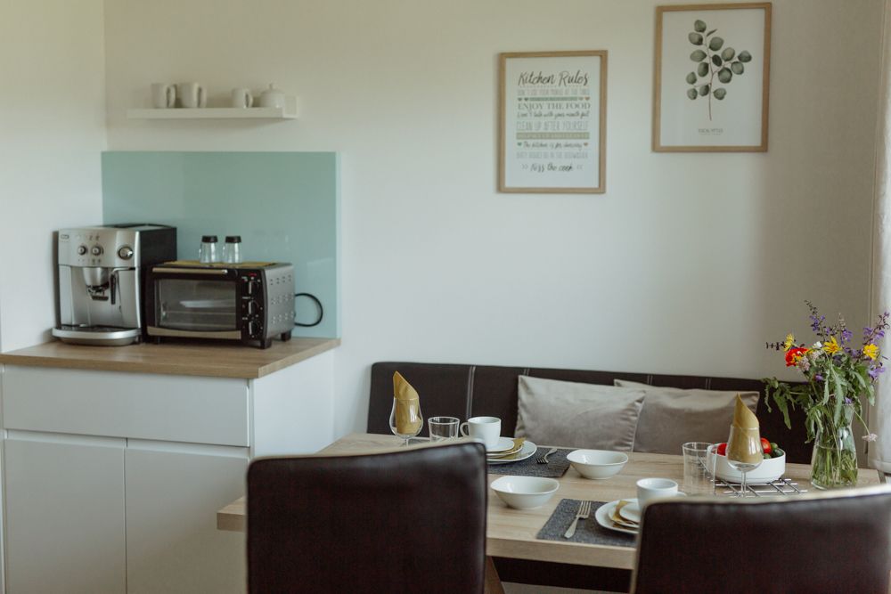 Malá kuchyňka s kávovarem, troubou, jídelním stolem a květinami.