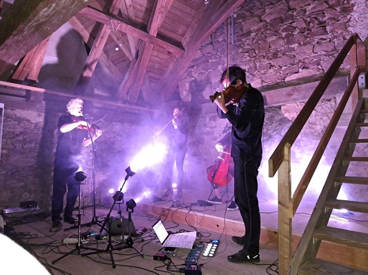 Hudebníci hrají v rustikálním podkroví se světelnými efekty.